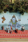 People gather on red steps before a mural of shiva