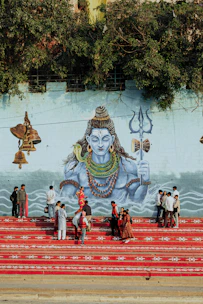 People gather on red steps before a mural of shiva