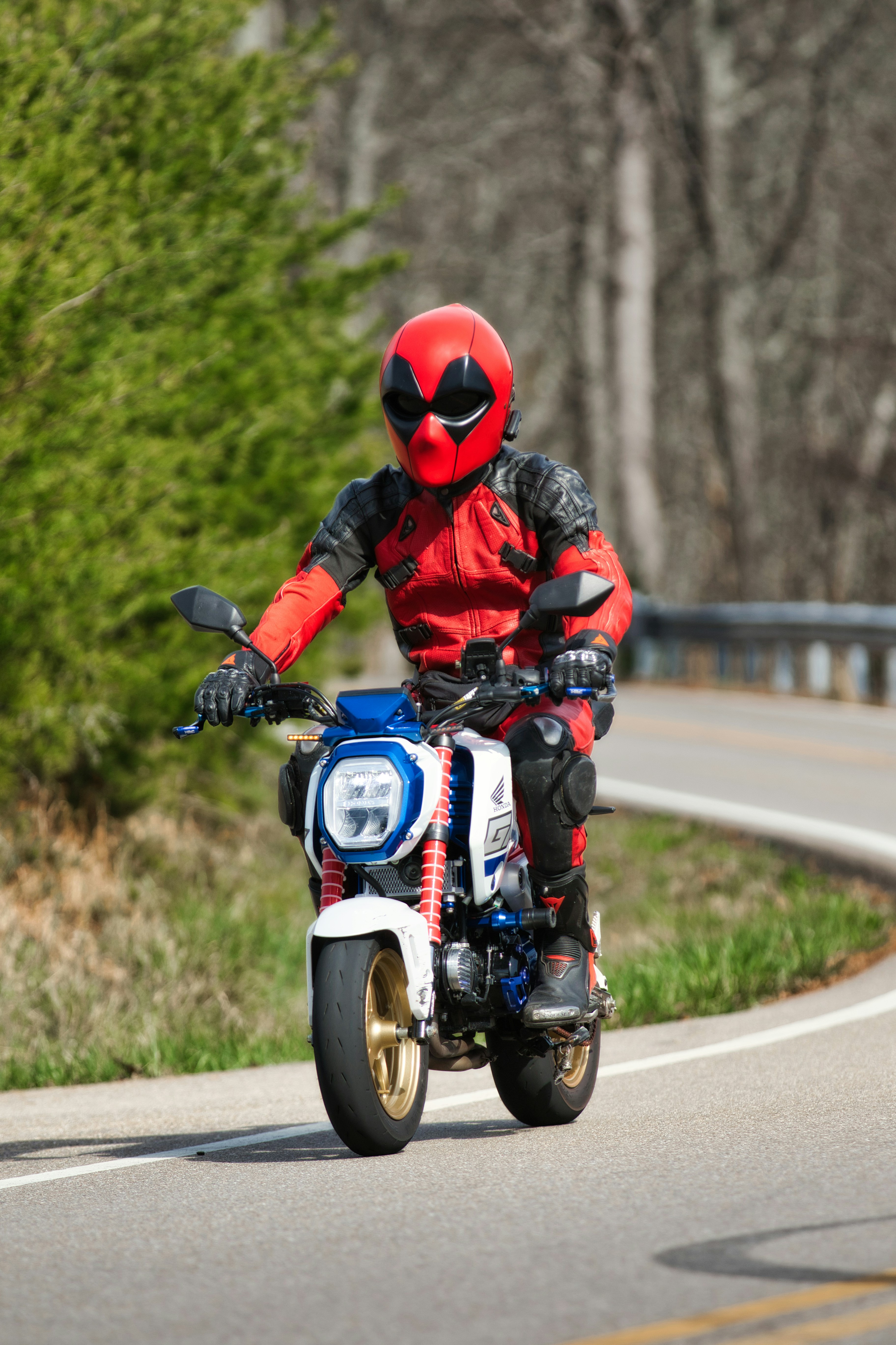 Orang dengan kostum deadpool mengendarai sepeda motor di jalan
