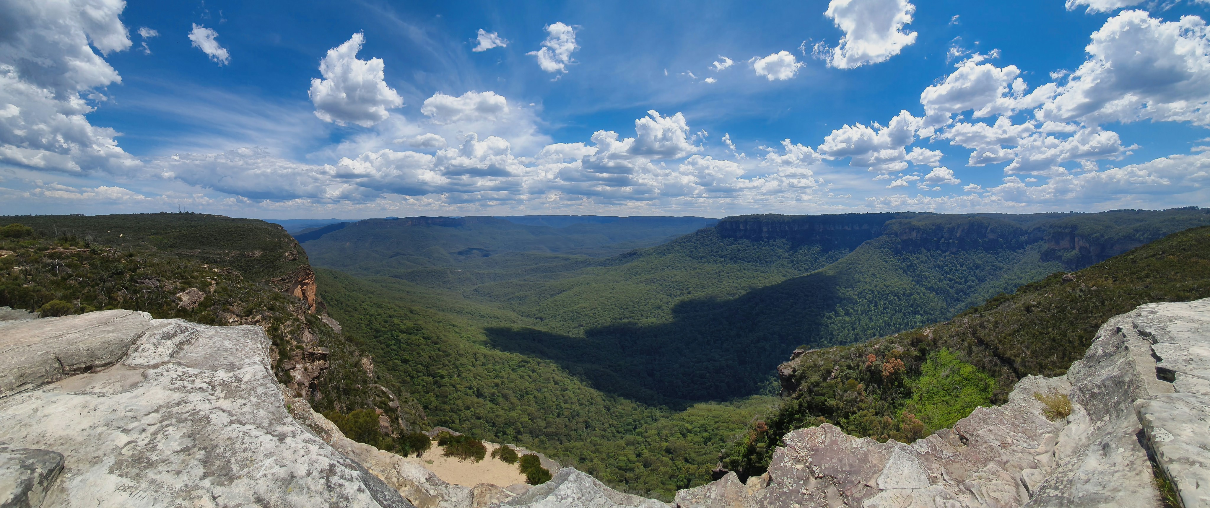 Vast green valley with rocky cliffs under blue sky.