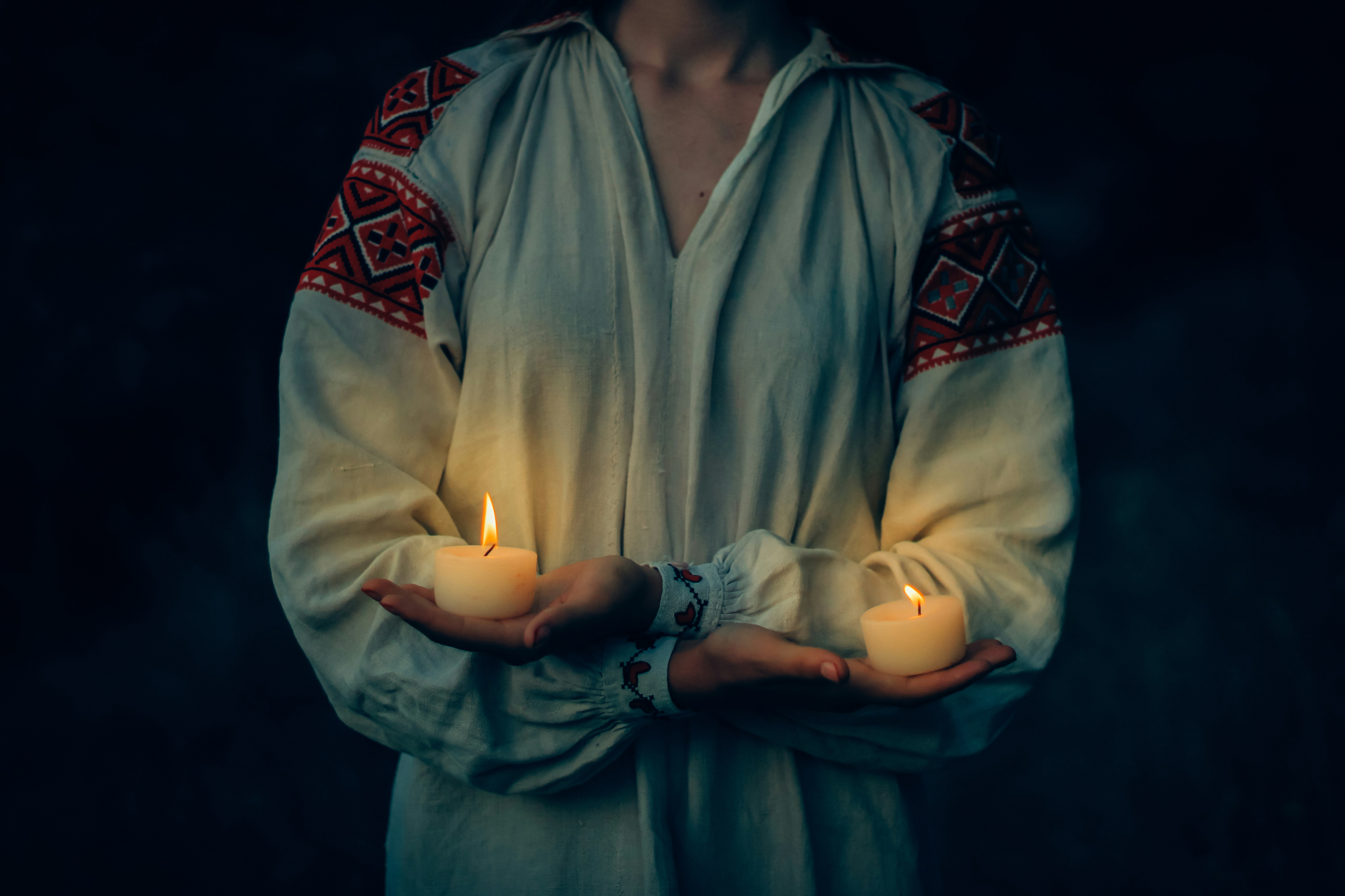 Person holding two lit candles in dark room
