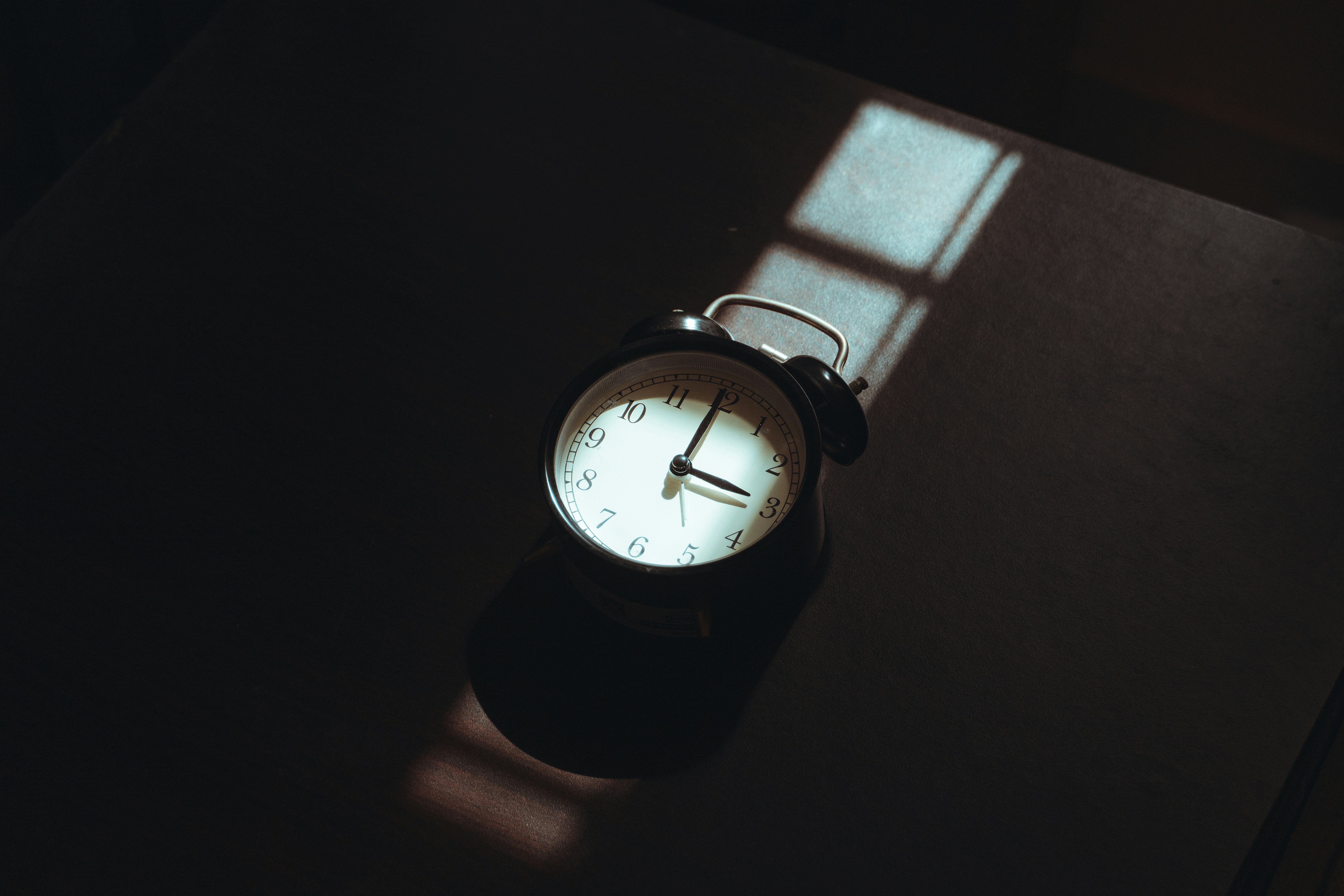 Alarm clock casting a shadow on a dark surface.