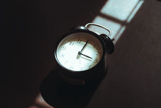 An alarm clock casts a shadow on a dark surface.