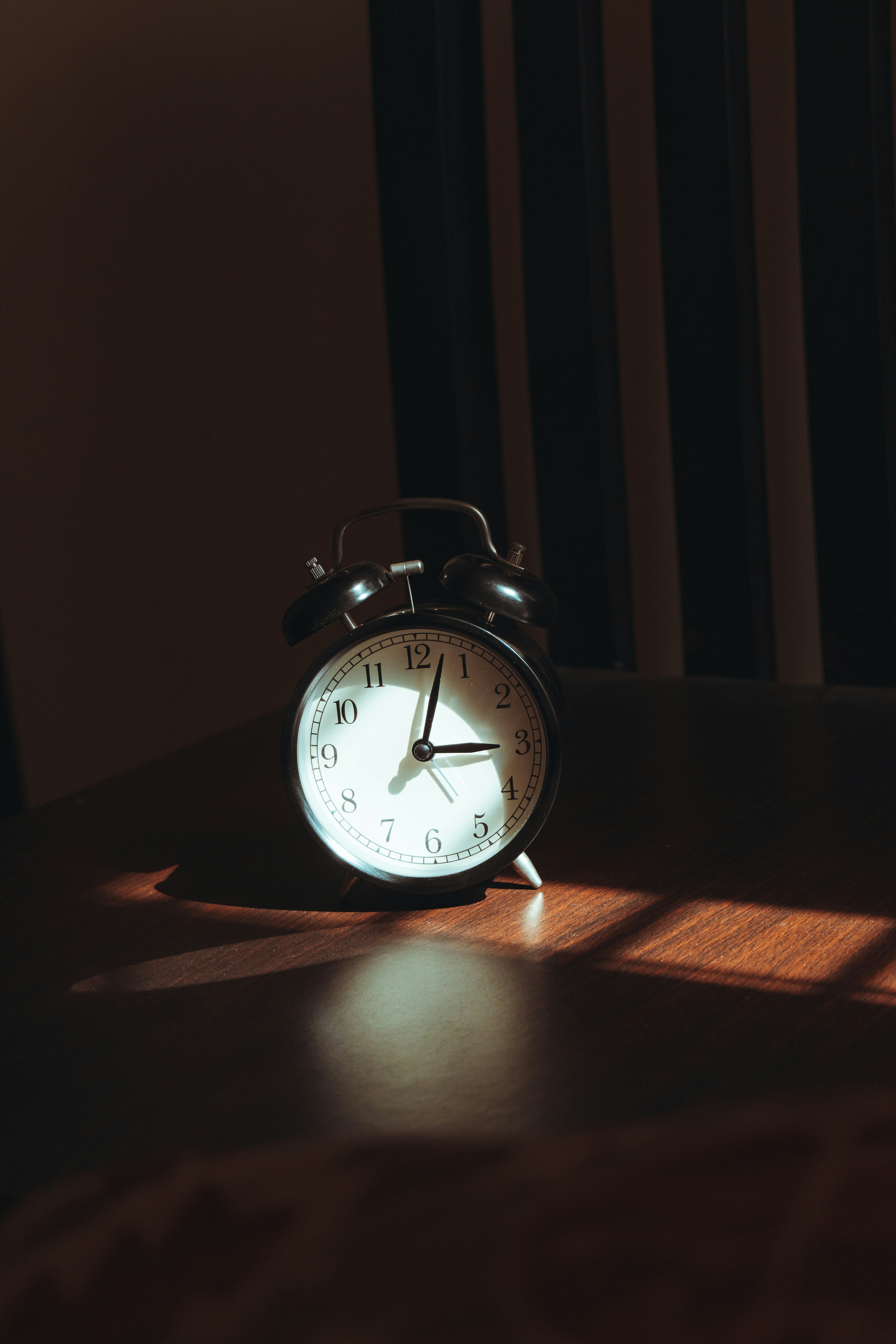 An old alarm clock sits on a wooden table.
