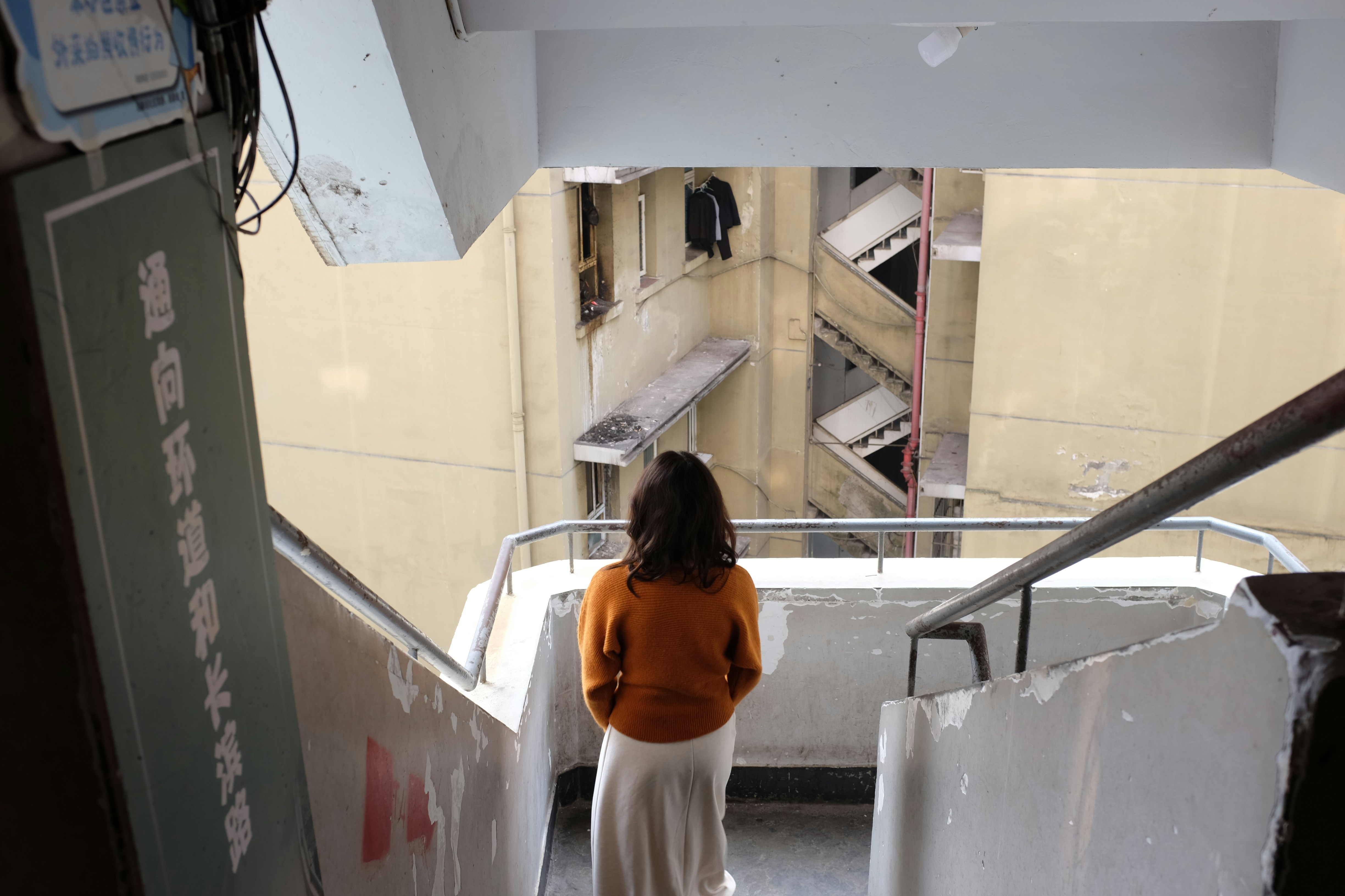 Woman in orange sweater looking down stairwell.
