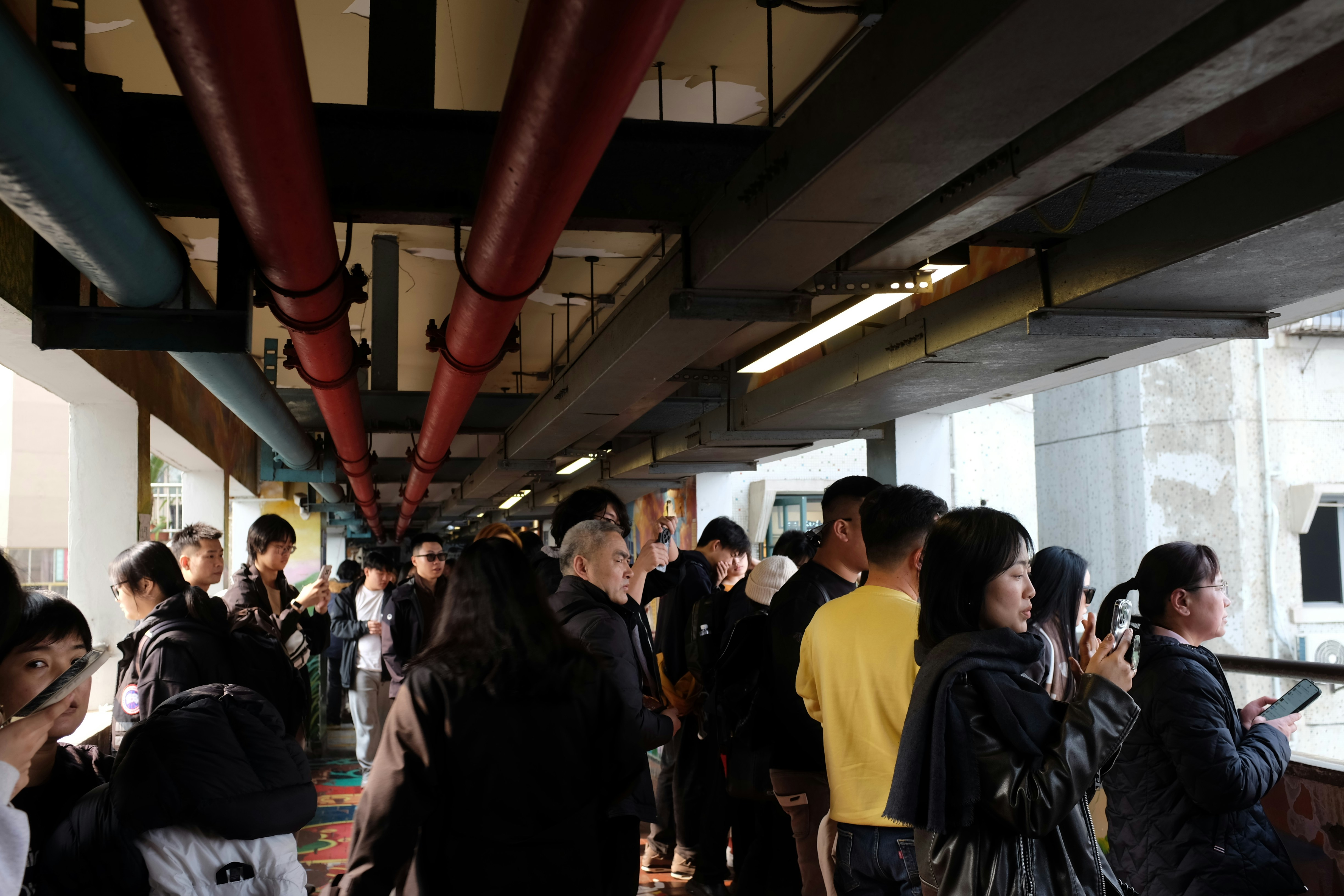 People gathered under pipes in an urban walkway.