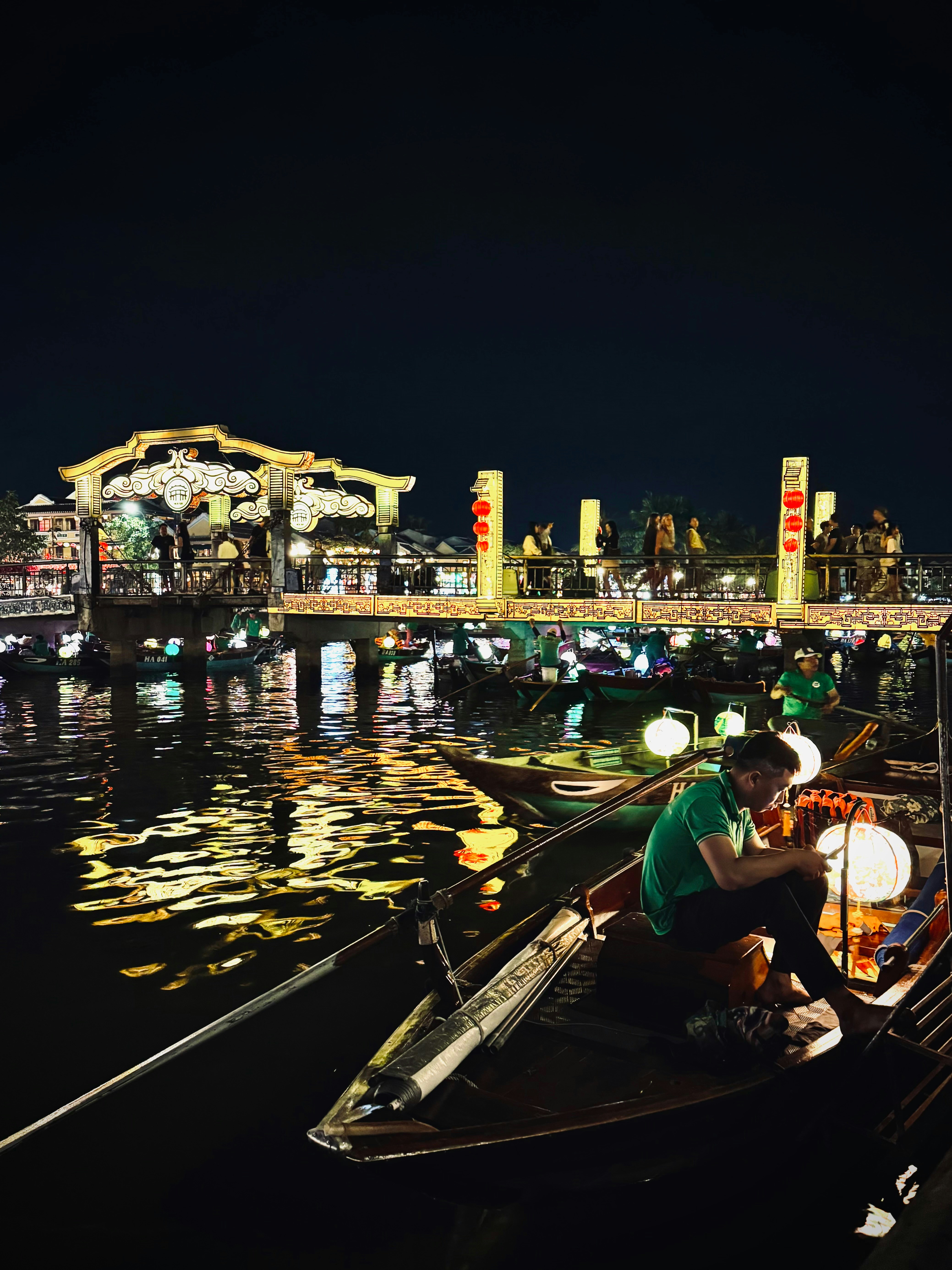 Boats on a river at night with a lit bridge.