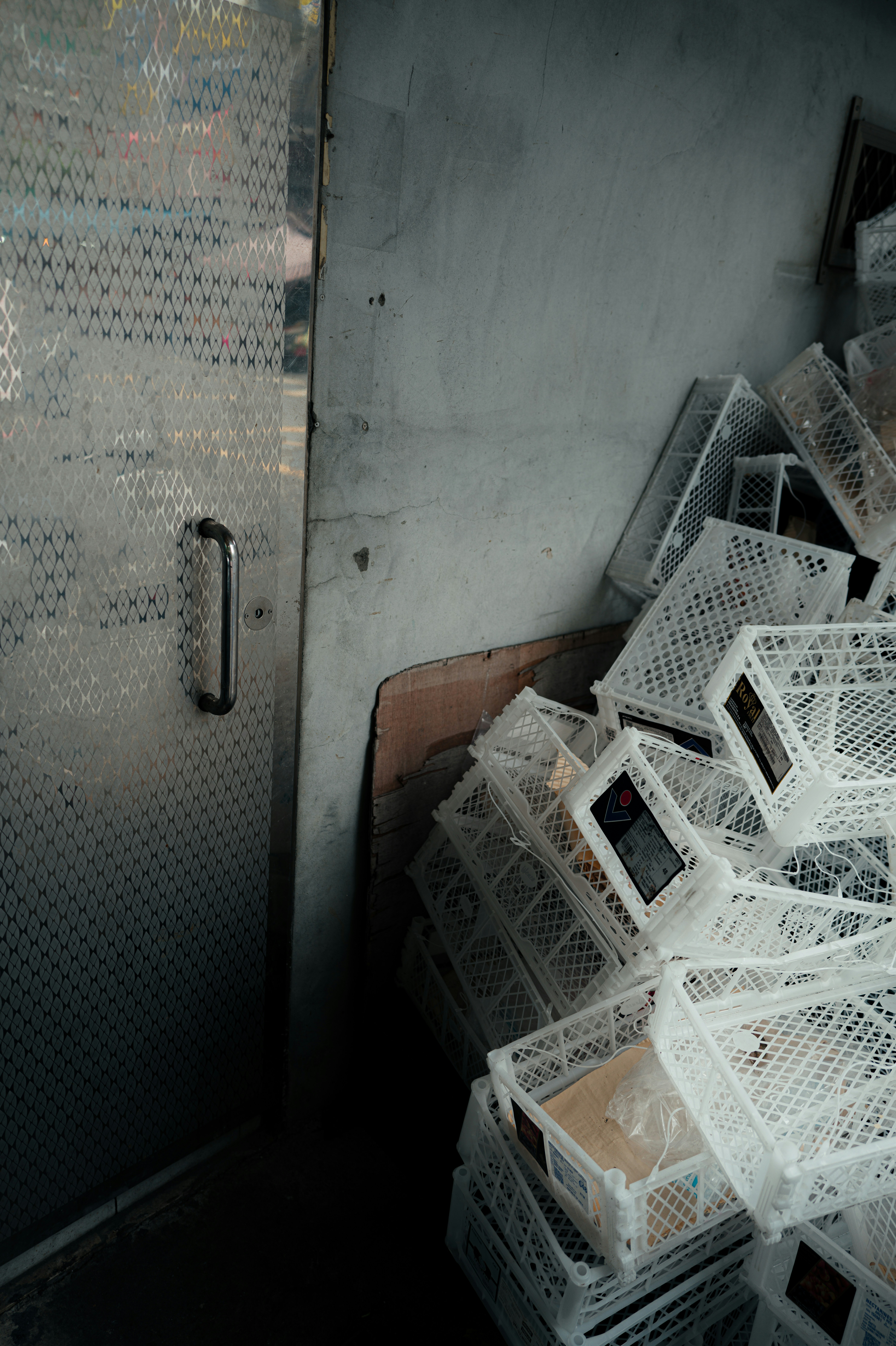 Pilha de caixas plásticas brancas ao lado de uma porta de metal.