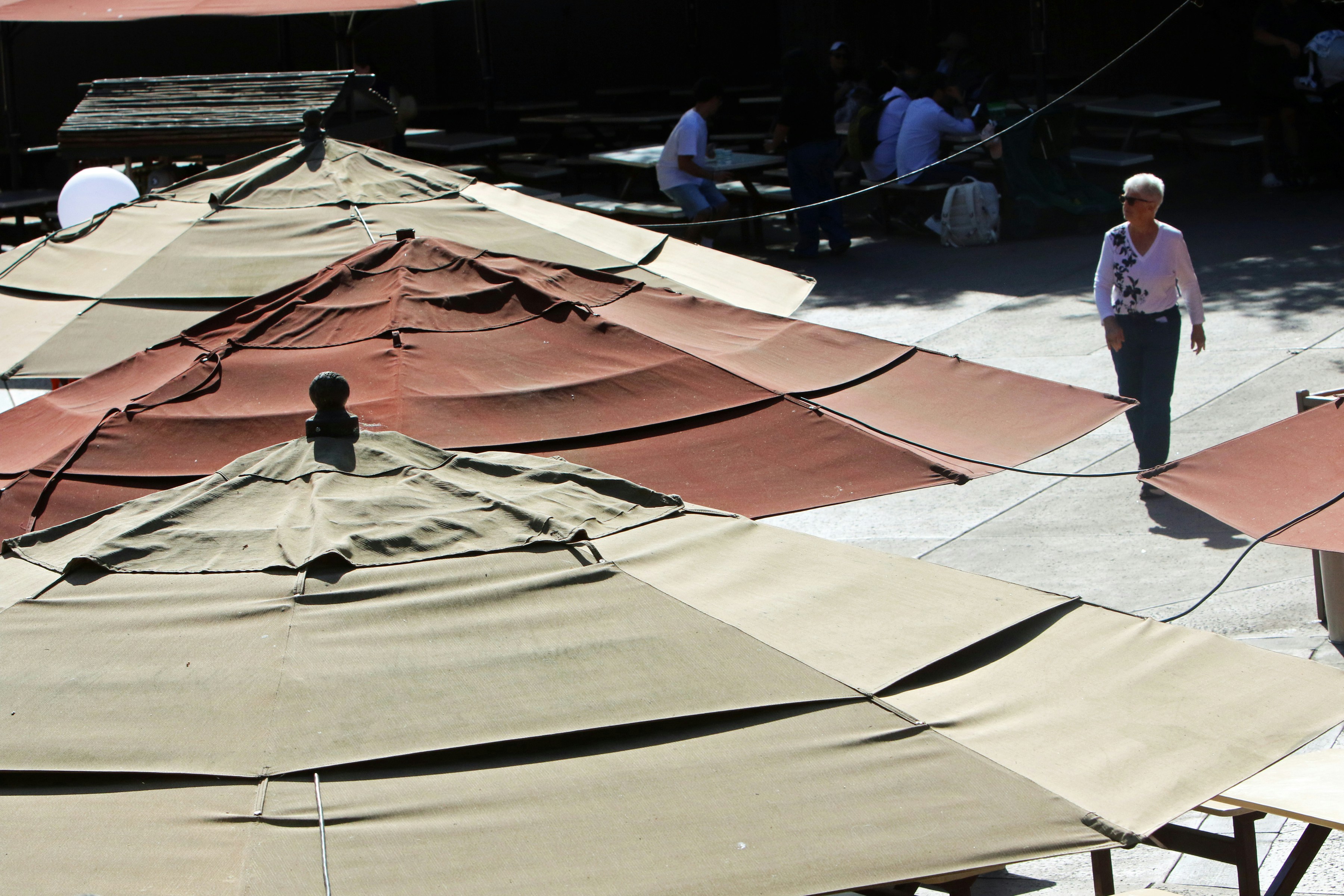 Una donna passa accanto a ombrelli da caffè all'aperto in una giornata di sole