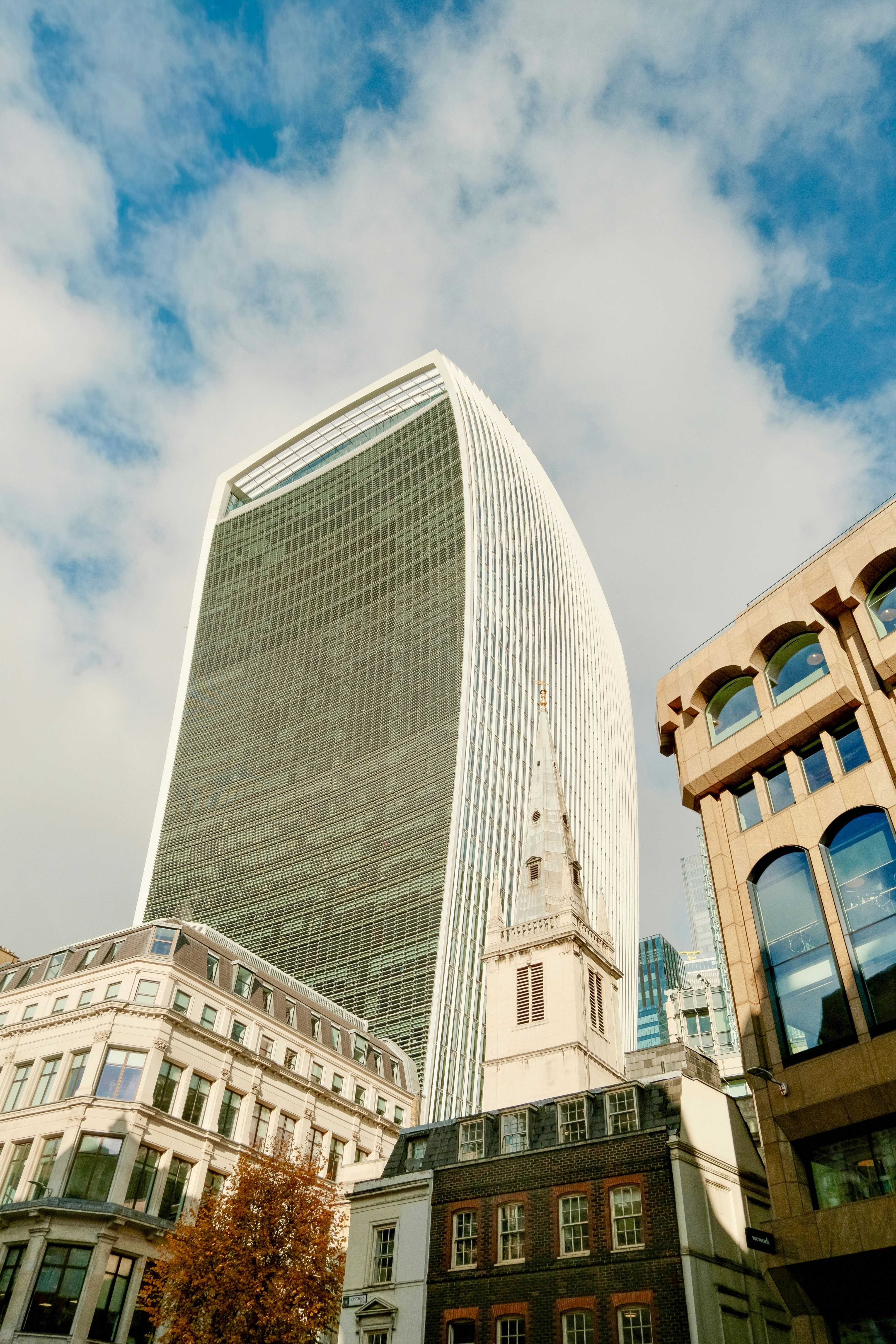 Modern skyscraper alongside historic buildings under cloudy sky