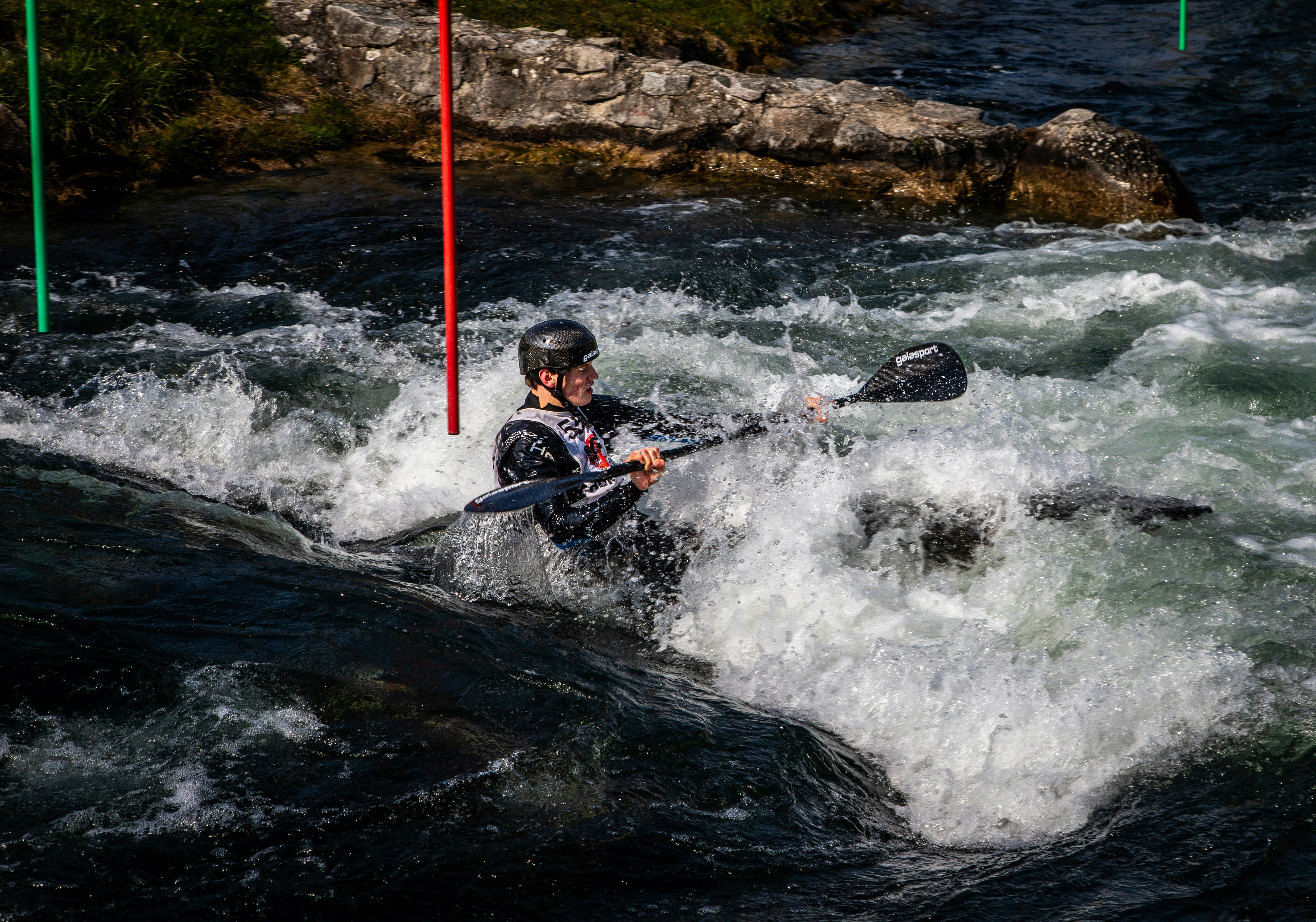 Kayaker navigates turbulent rapids with gates.