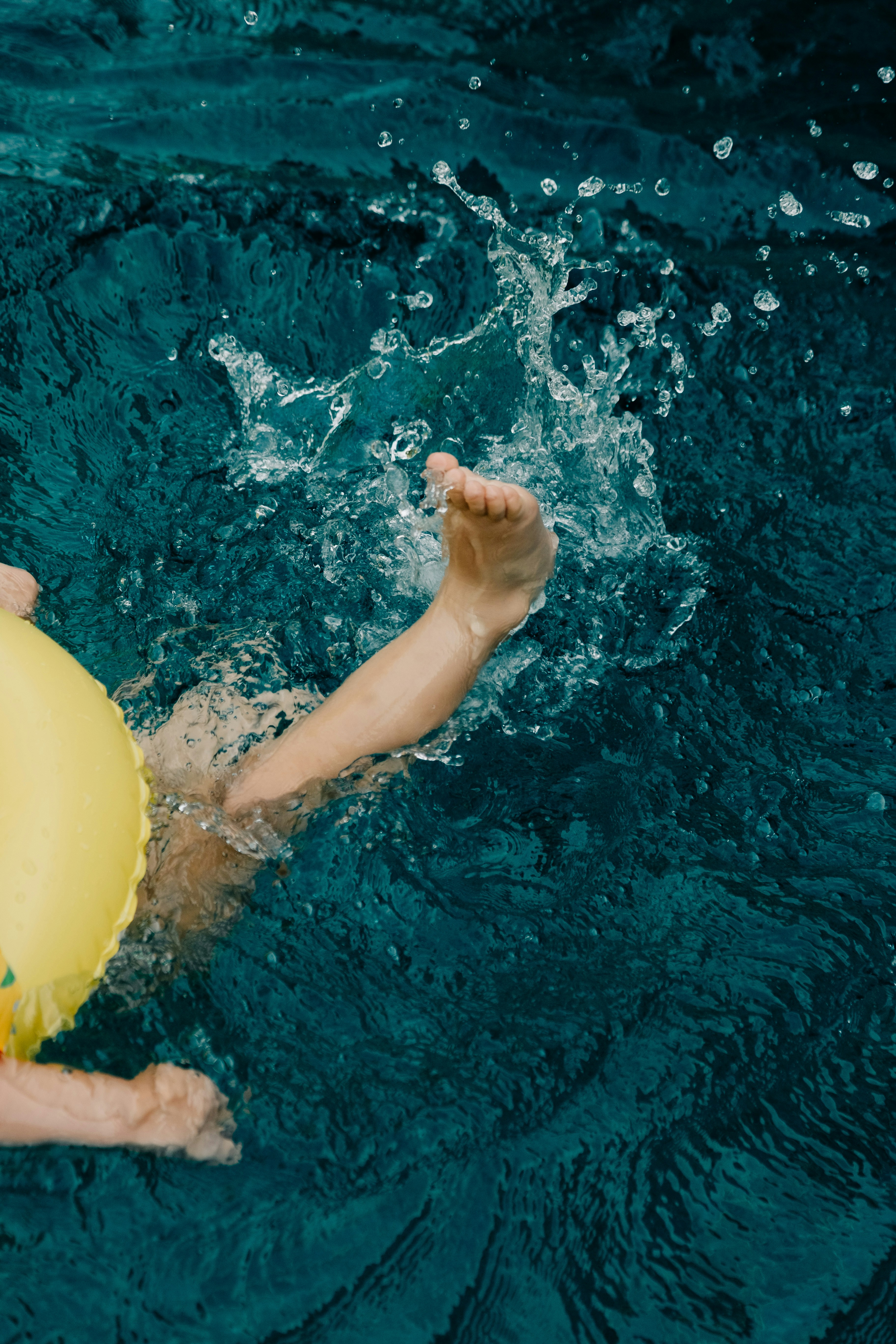 Child's legs splashing in blue water with yellow float.