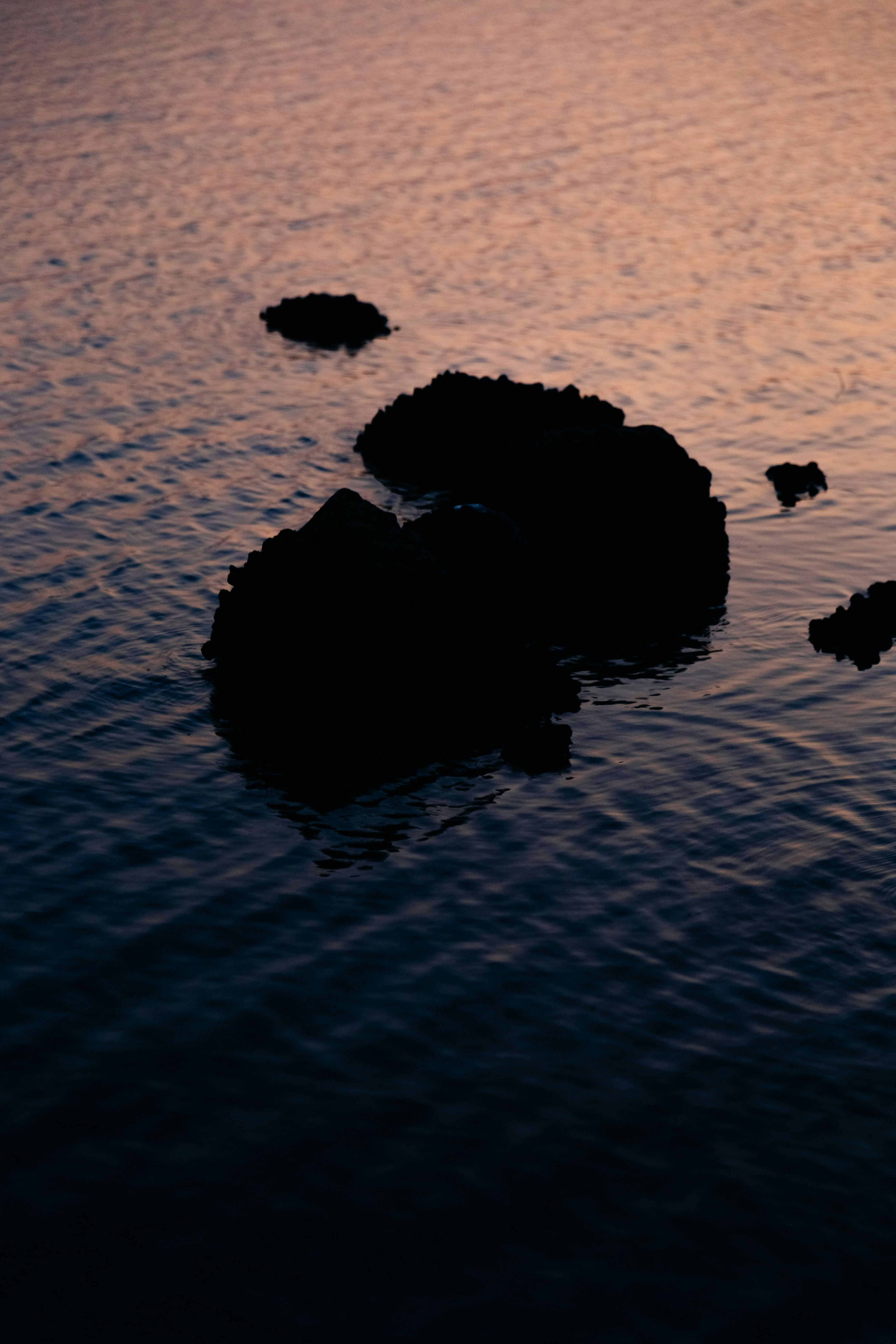 Rochas silhuetas em águas calmas do oceano ao pôr do sol