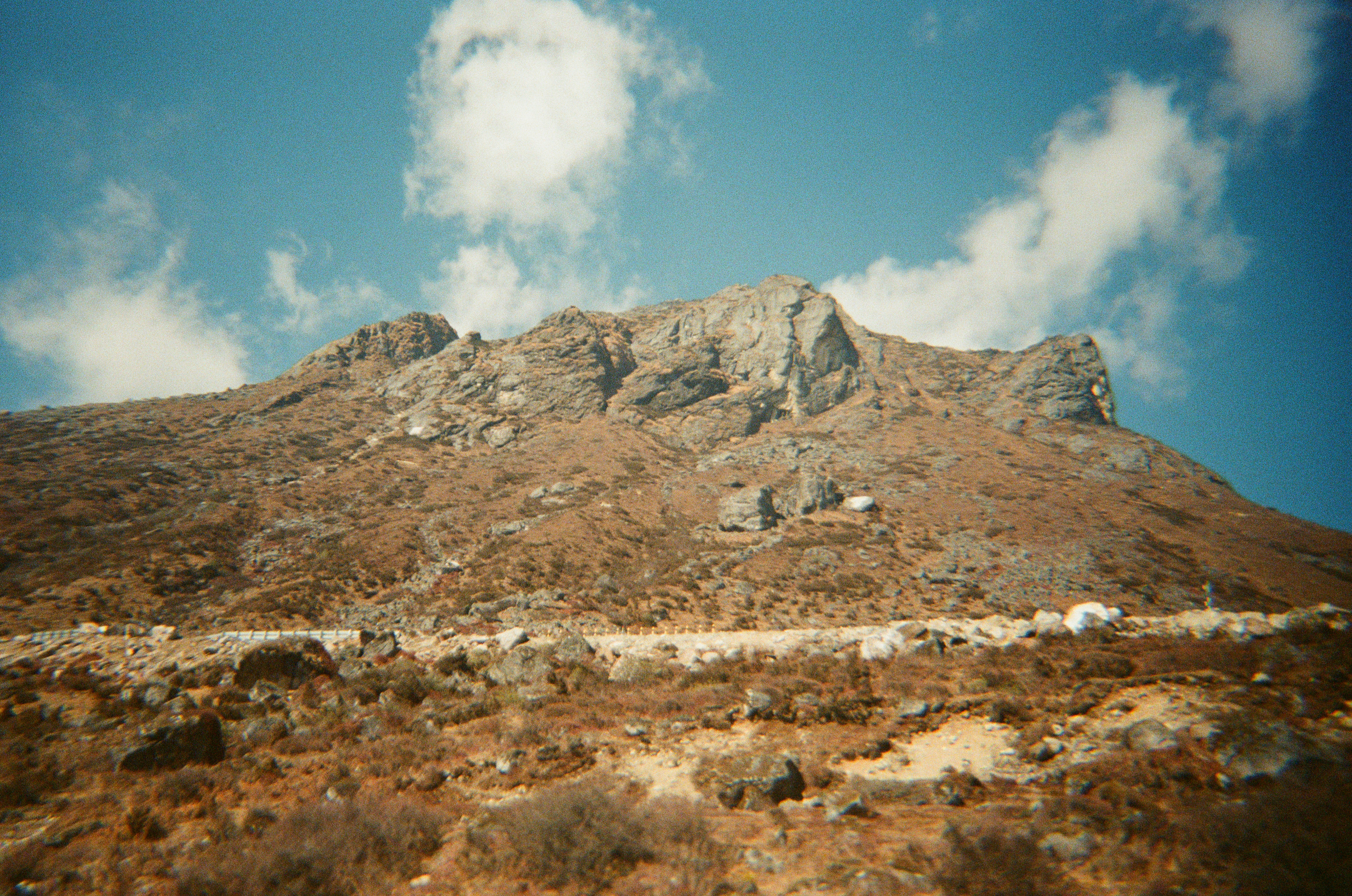 Rocky mountain slope with sparse vegetation under a blue sky.