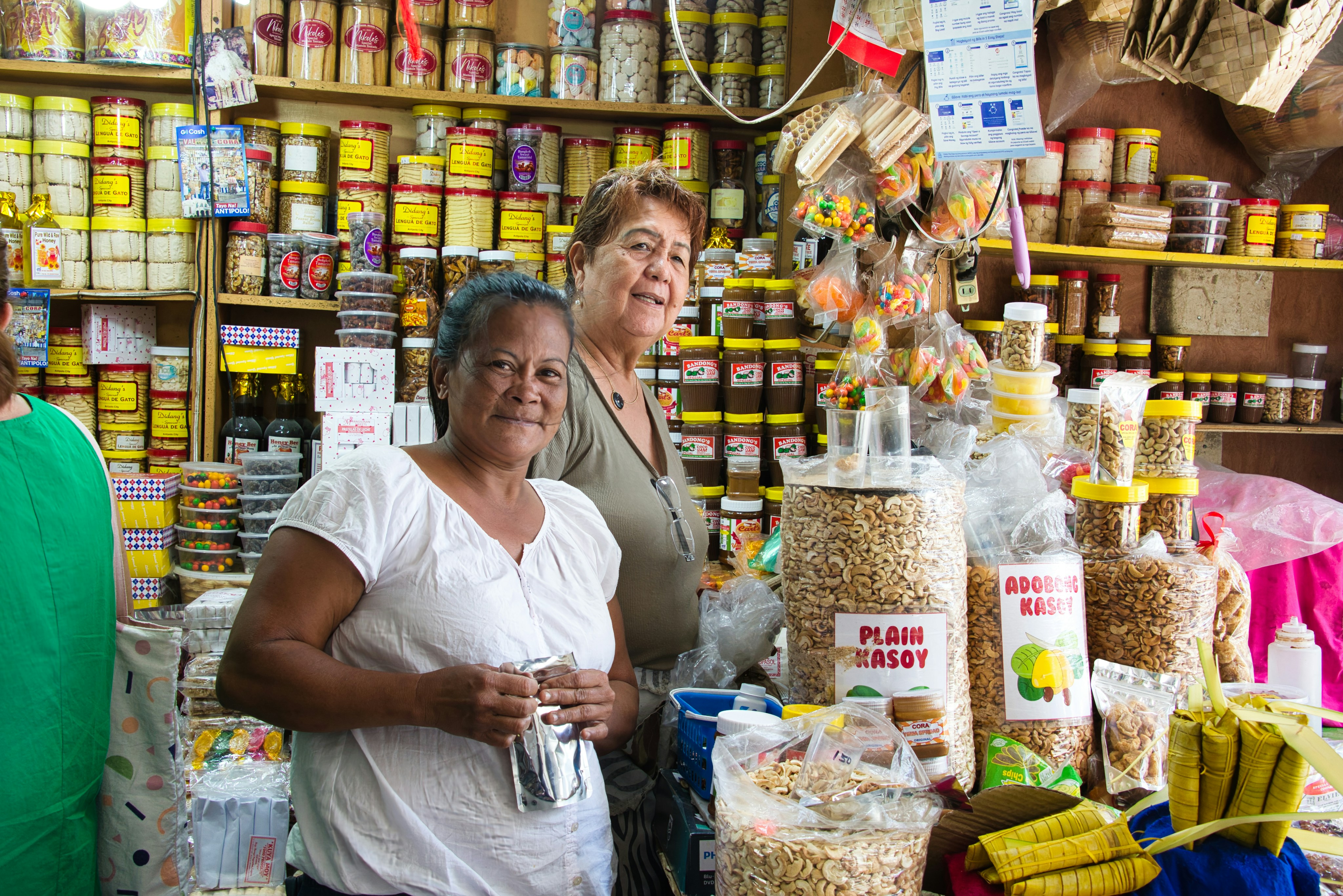 two women in a market stall with food items smiling