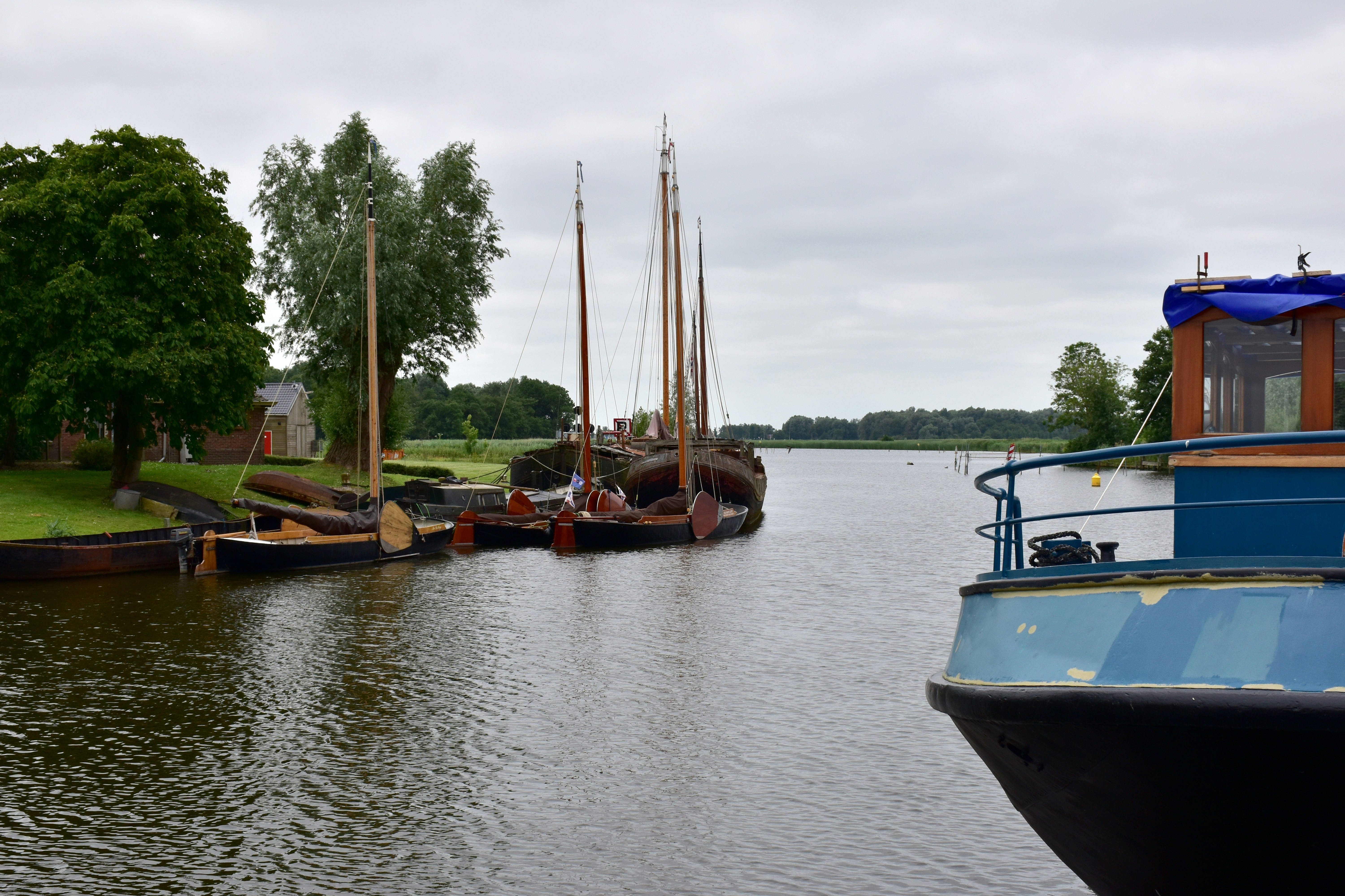 Sailboats docked on a calm river under cloudy sky