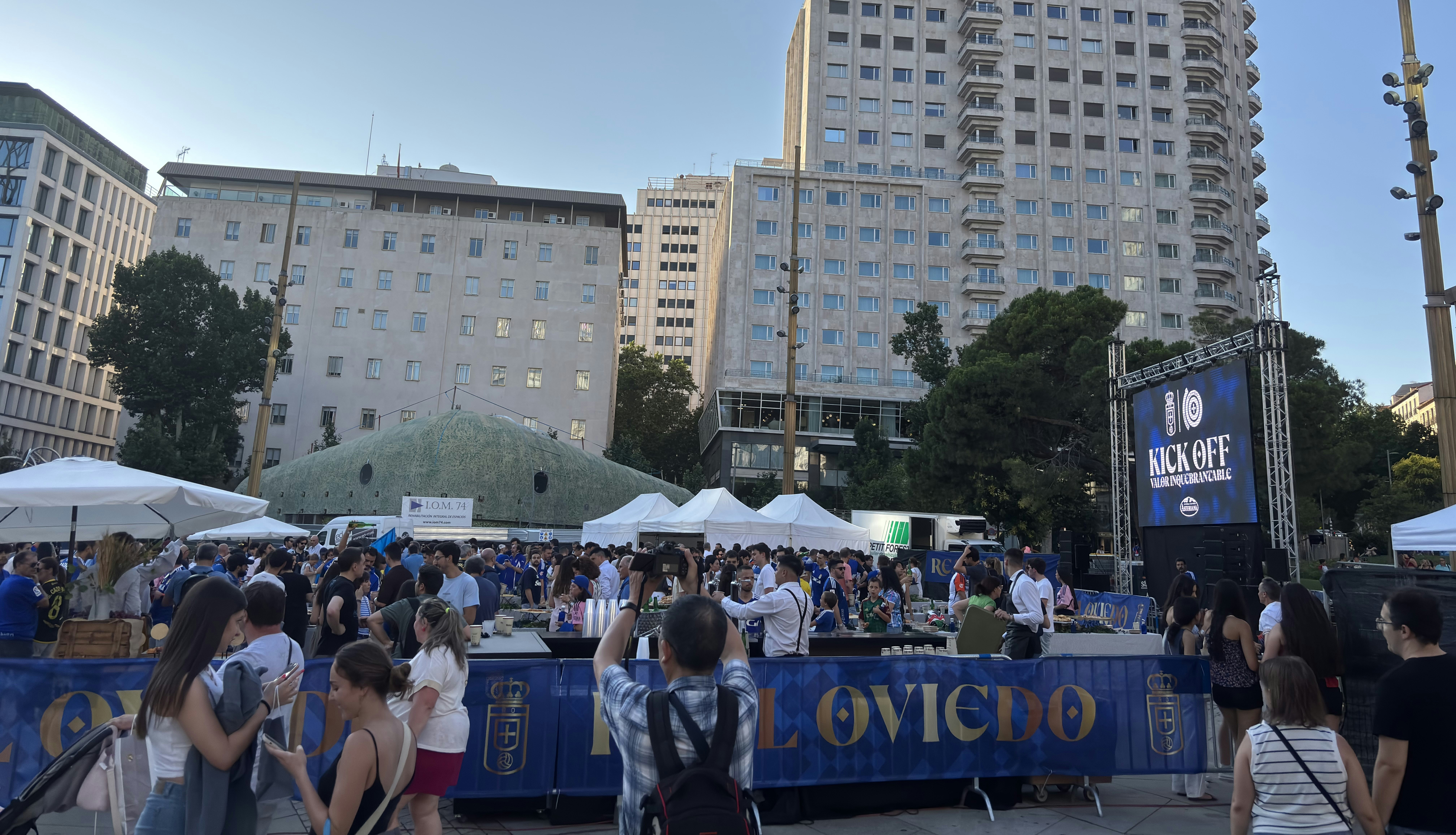 Crowd gathered at an outdoor event with tents and buildings.