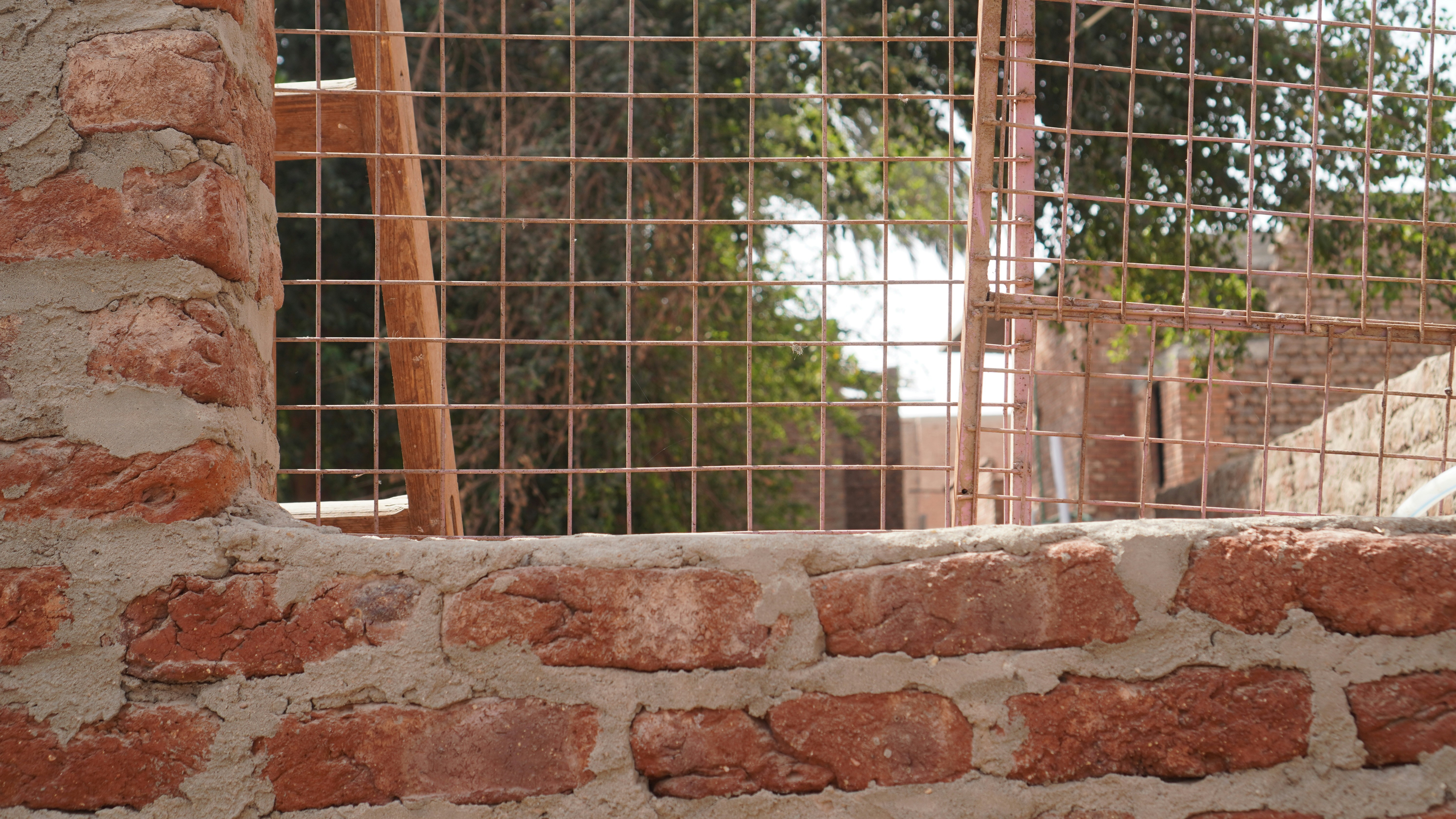 Brick wall with a wire mesh fence behind it.