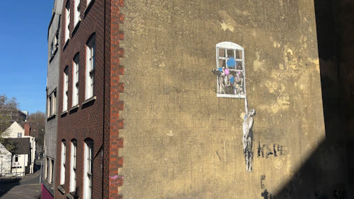 Street art of a figure hanging from window