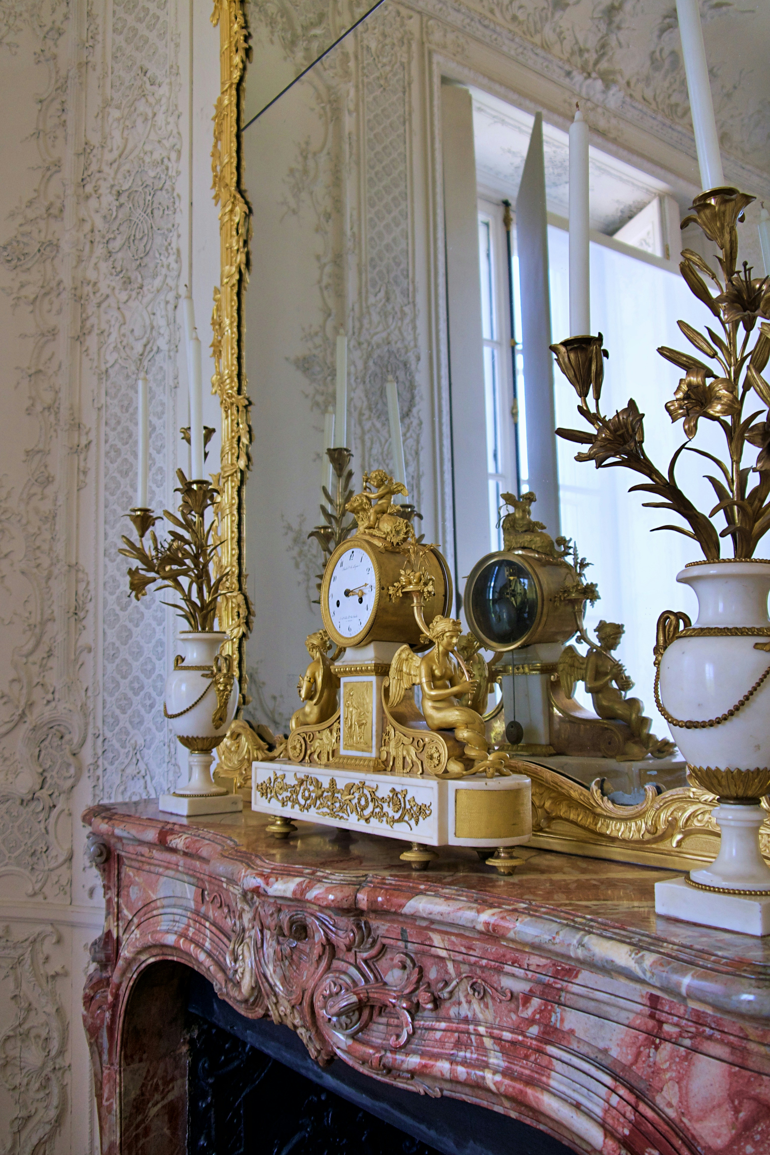 Relógio dourado ornamentado sobre uma lareira de mármore.