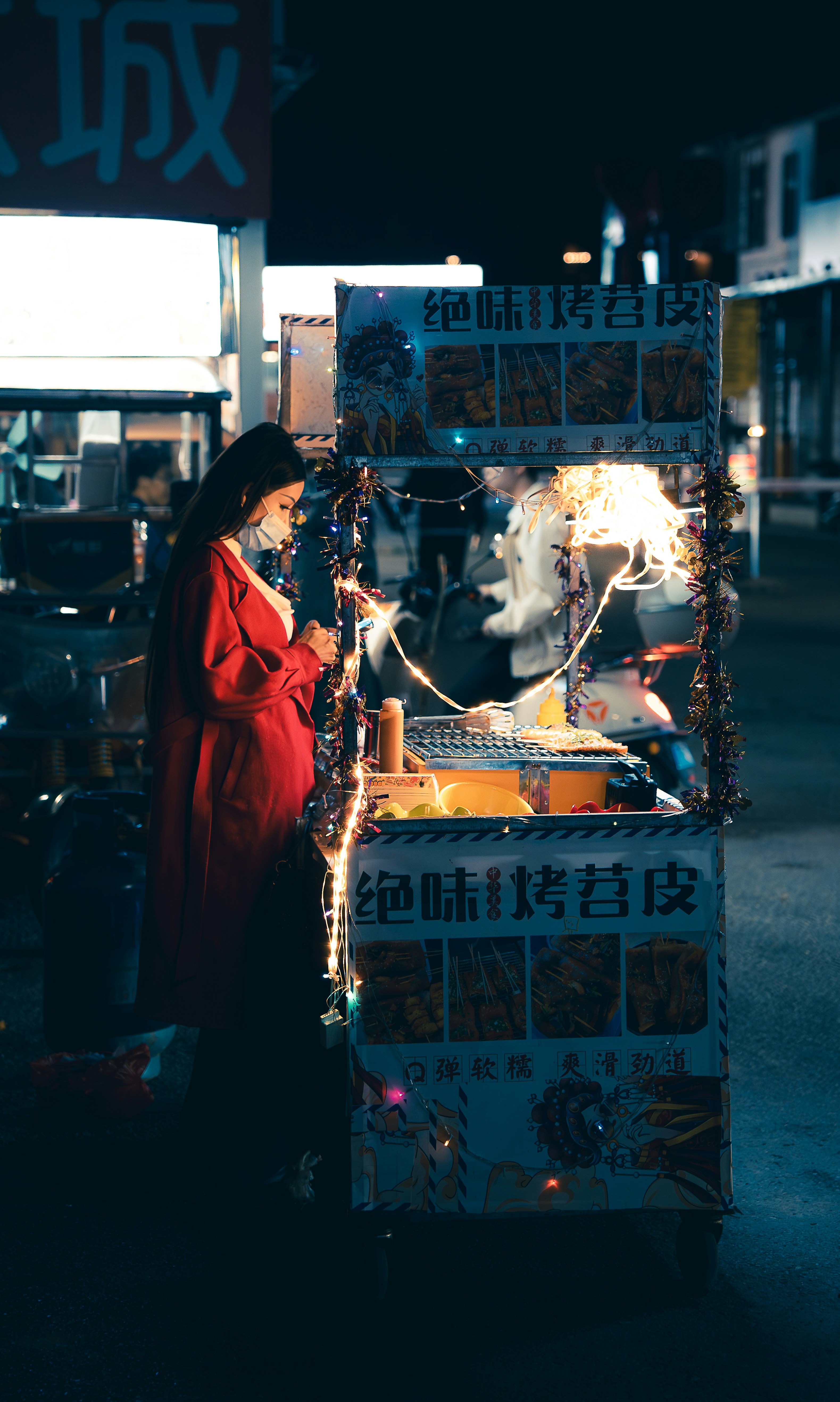 Mulher de vermelho preparando comida em uma barraca de mercado noturno.