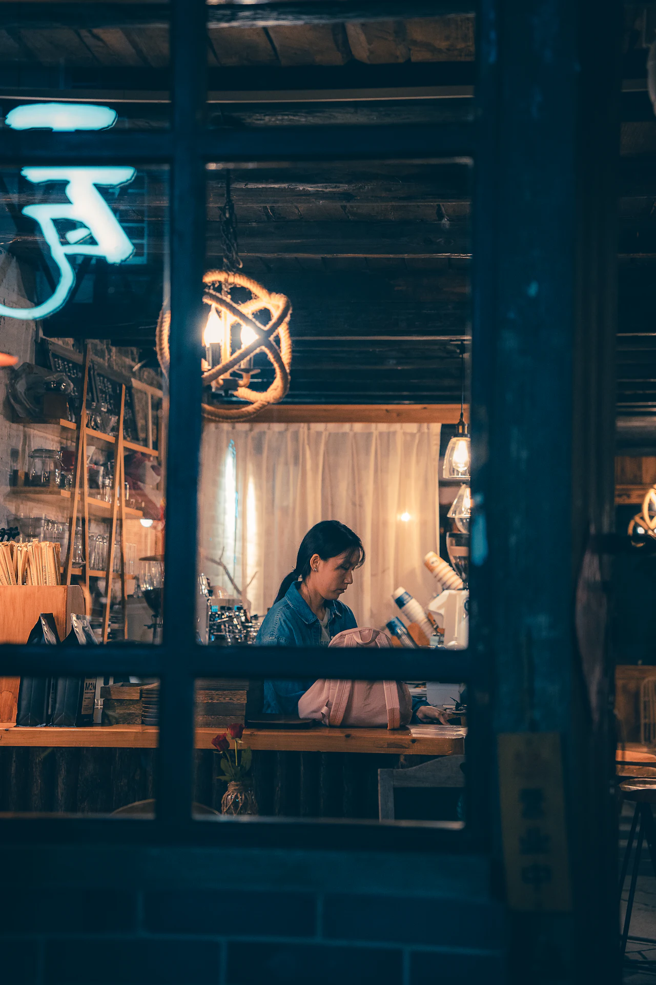 A woman seen through a window working at her own desk, absorbed in the task in front of her.
