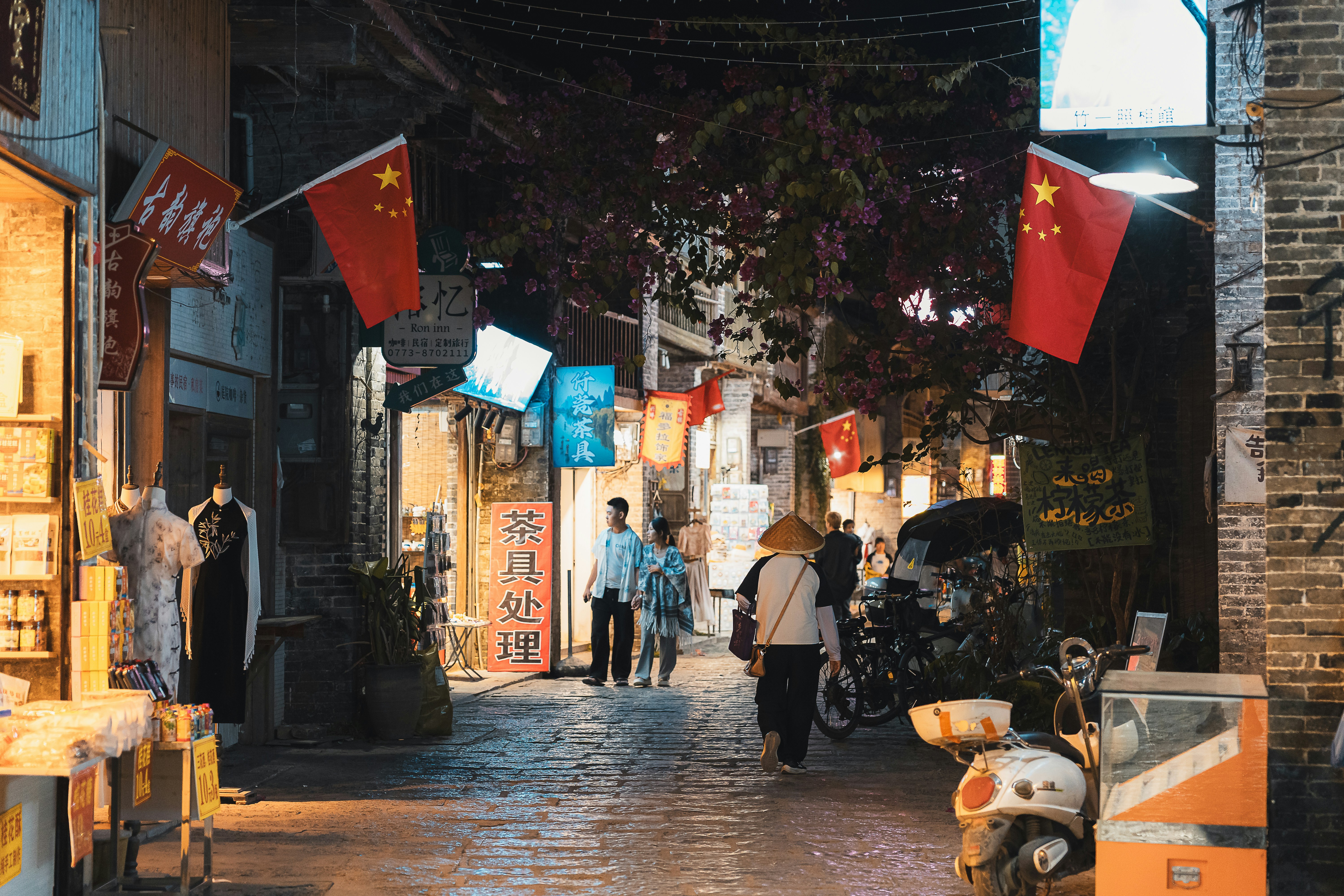 As pessoas caminham por uma rua estreita com bandeiras chinesas.