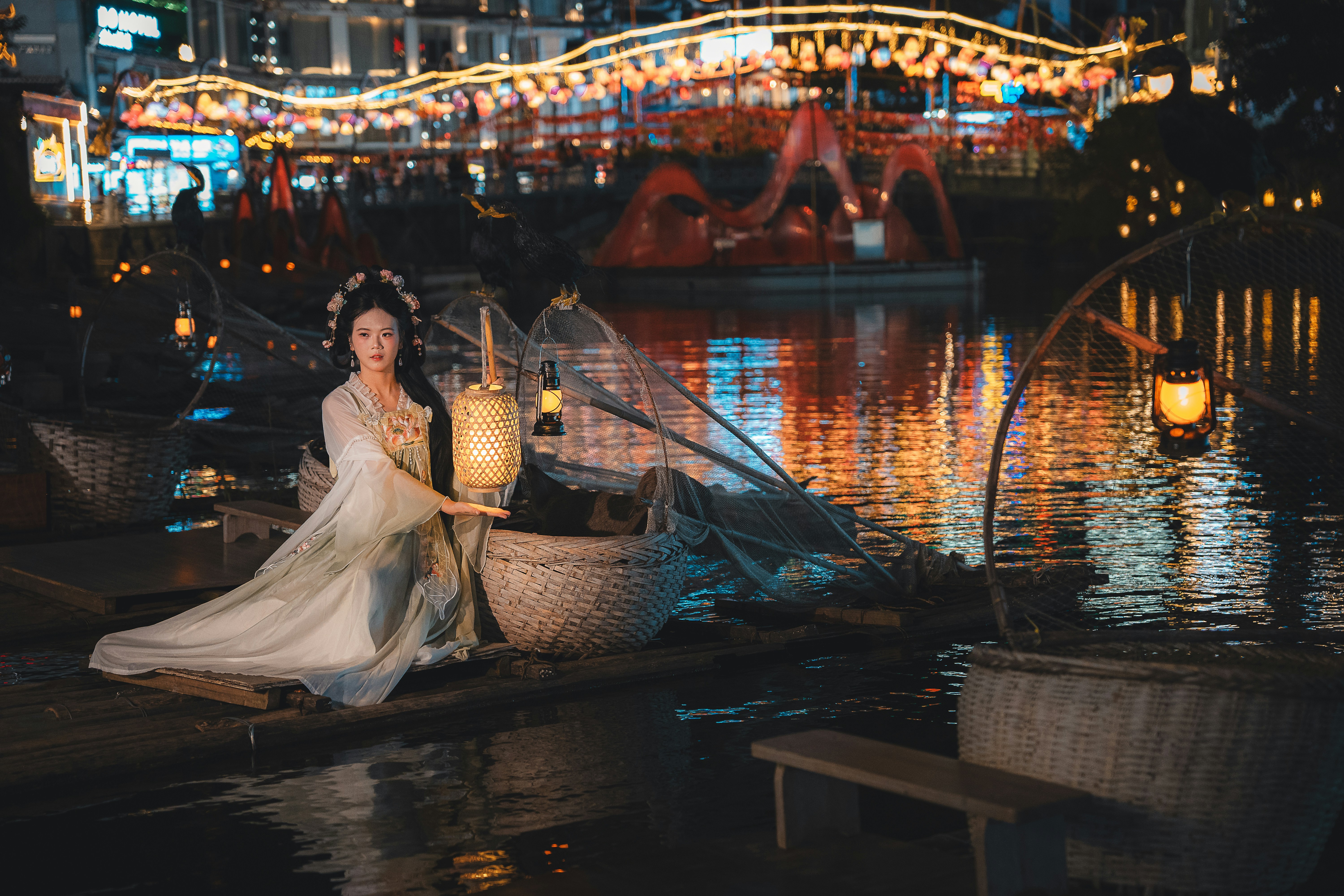 Mulher com traje tradicional segurando lanterna à beira da água à noite