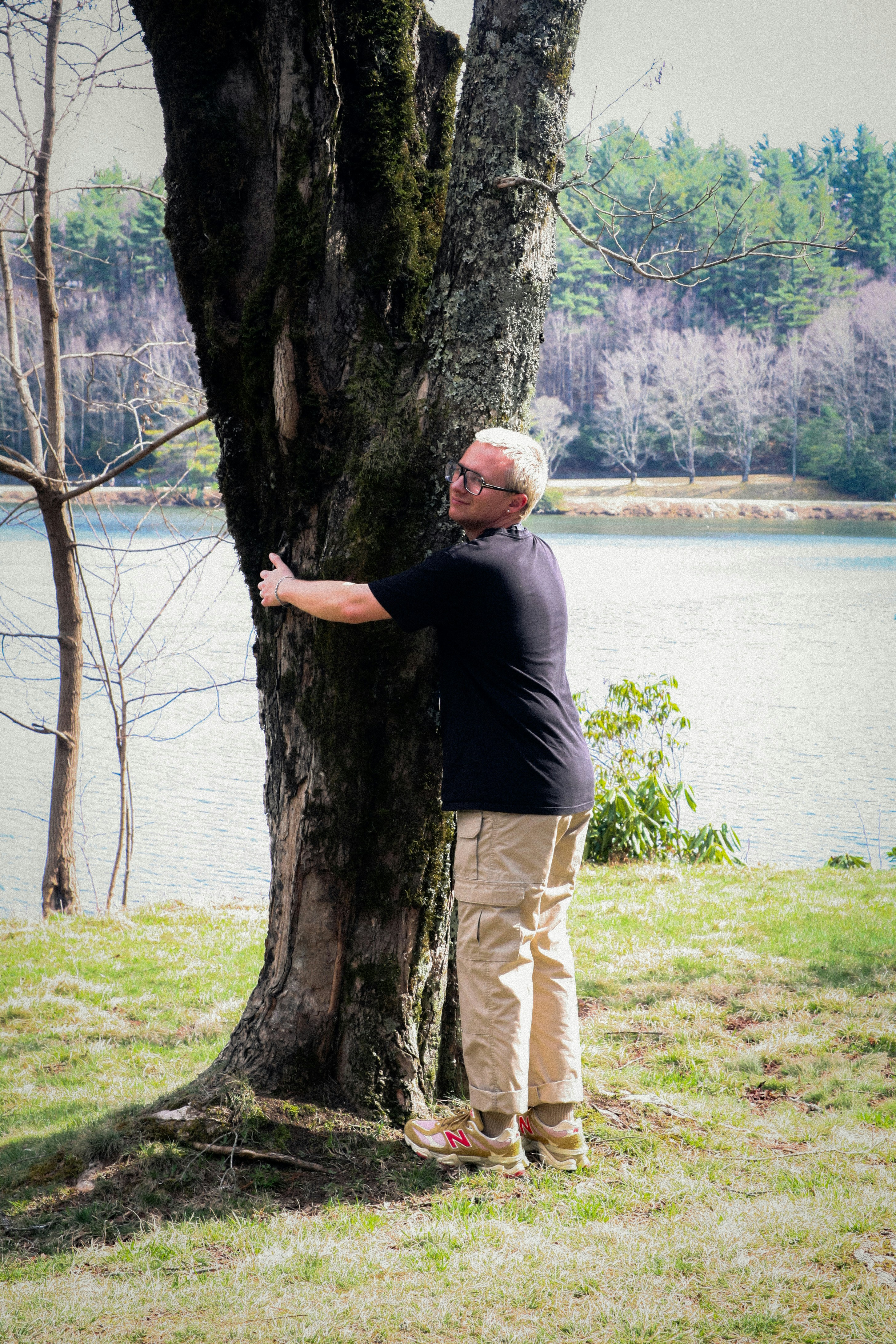 Hombre abrazado a un gran árbol junto a un lago