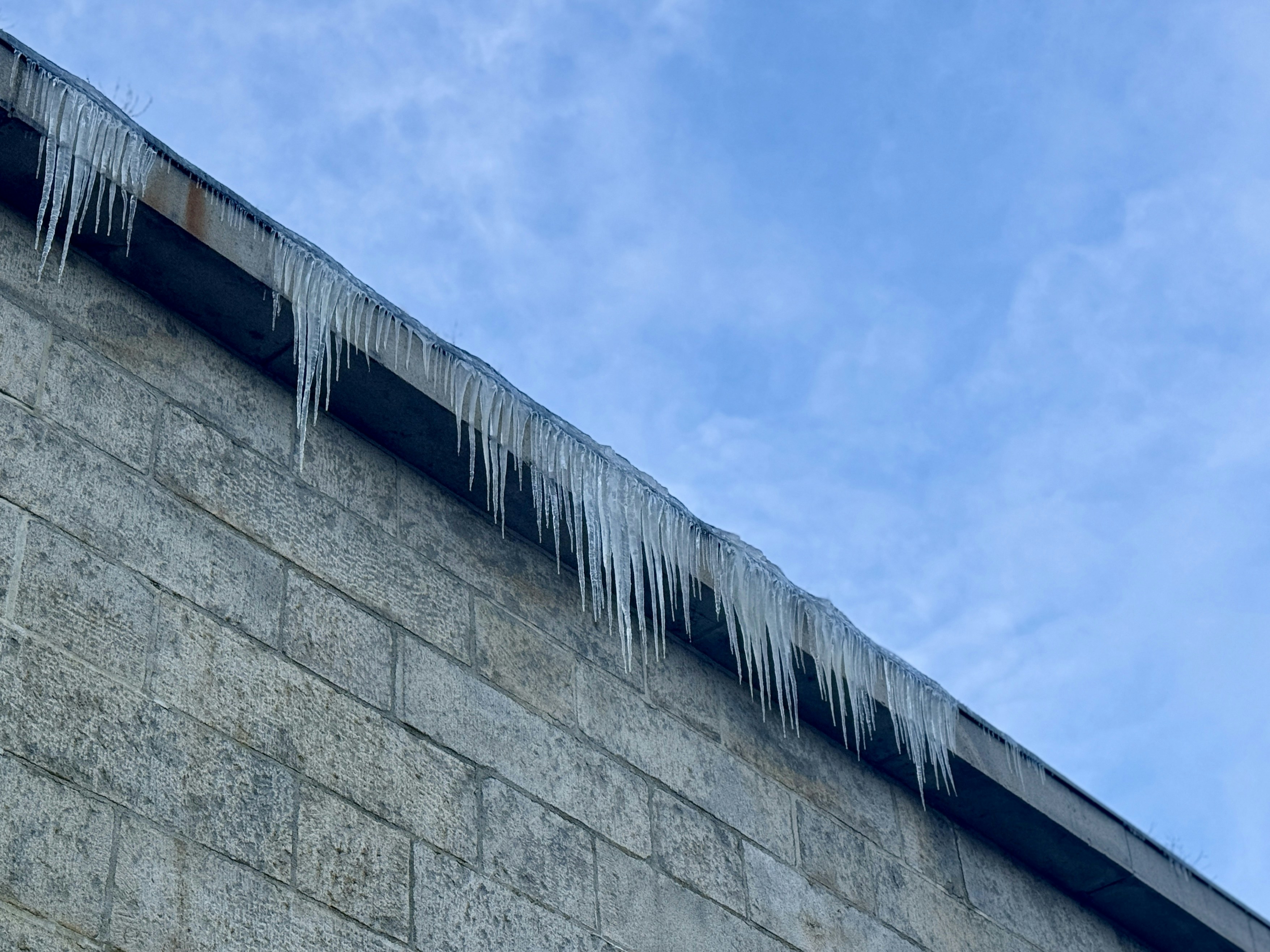 青空の下、建物の屋根から垂れ下がる氷柱