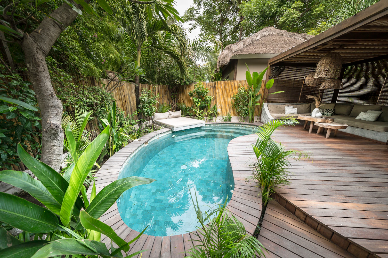 Piscina com deck de madeira e área de estar coberta cercada por vegetação.