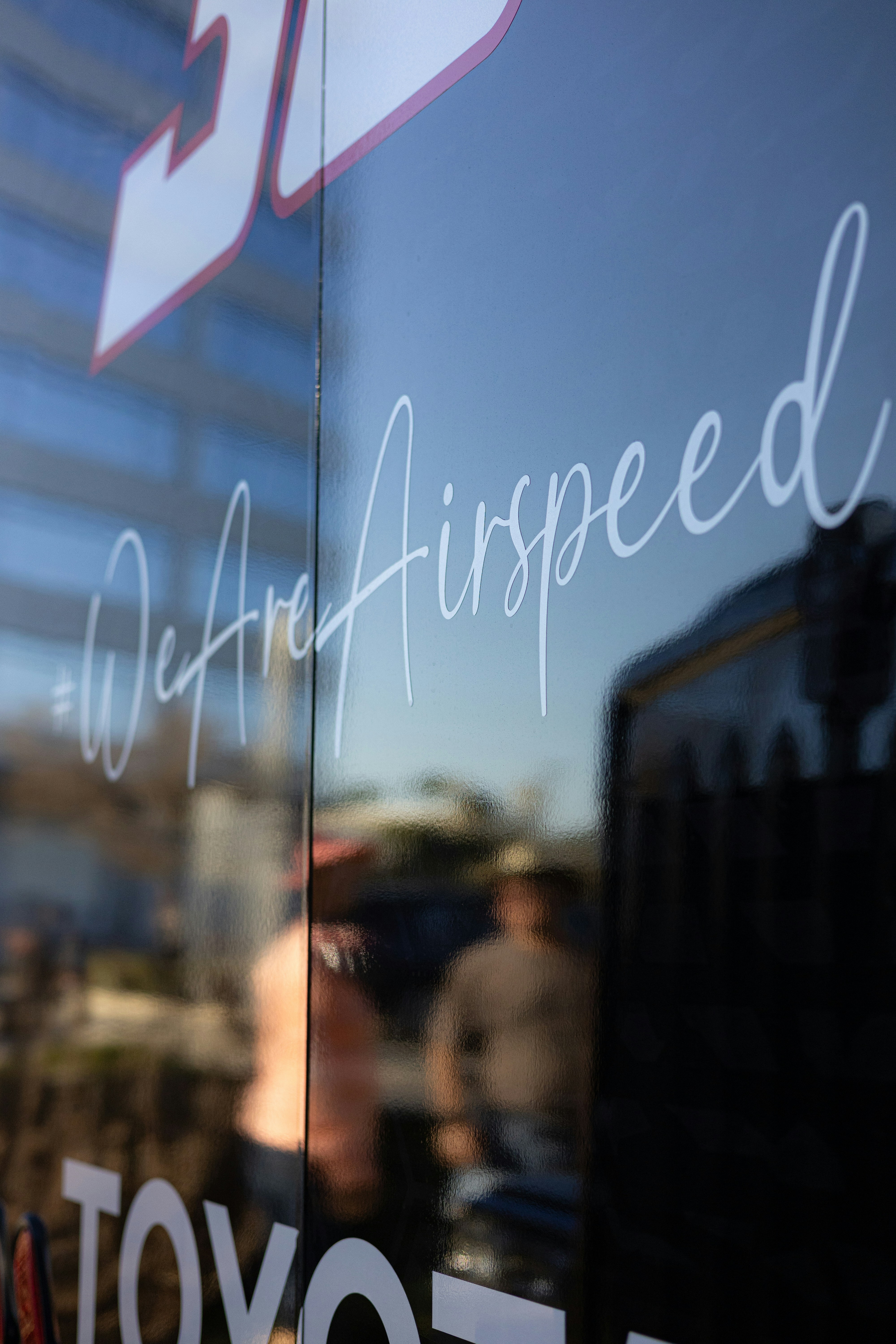 Reflexo das pessoas e "#weareairspeed" no vidro.