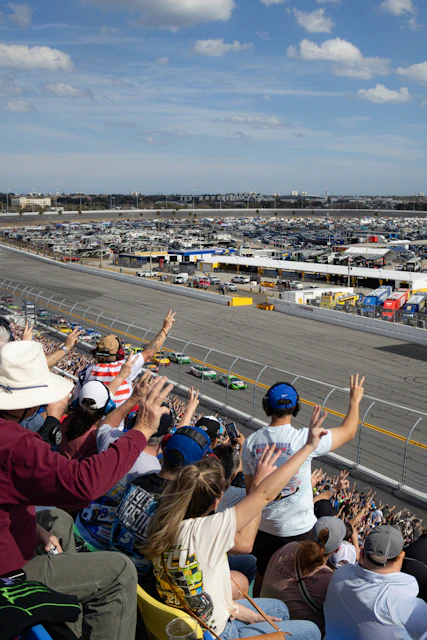 Spectators cheer at a nascar race on a sunny day.