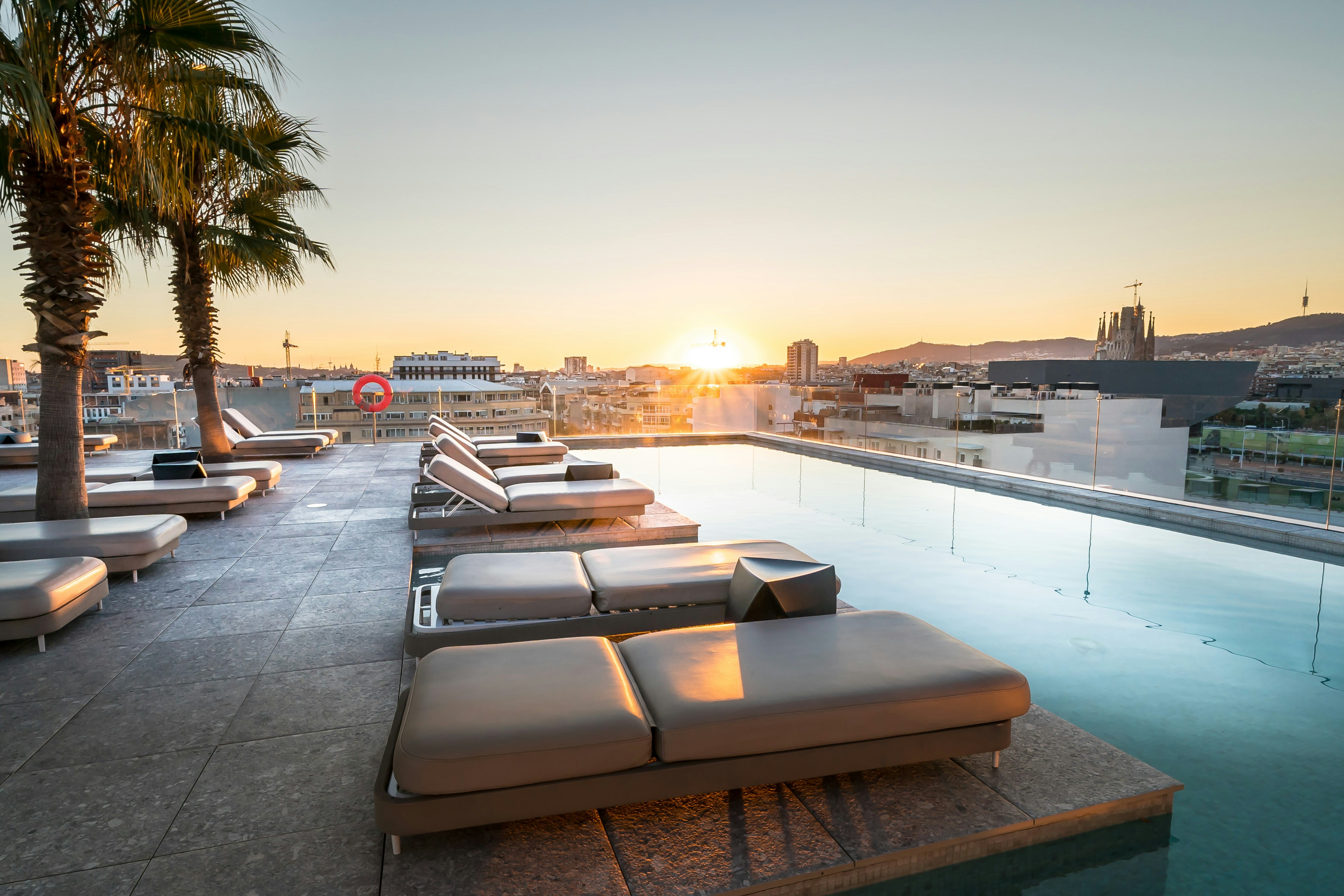 Rooftop pool and lounge chairs at sunset overlooking city.