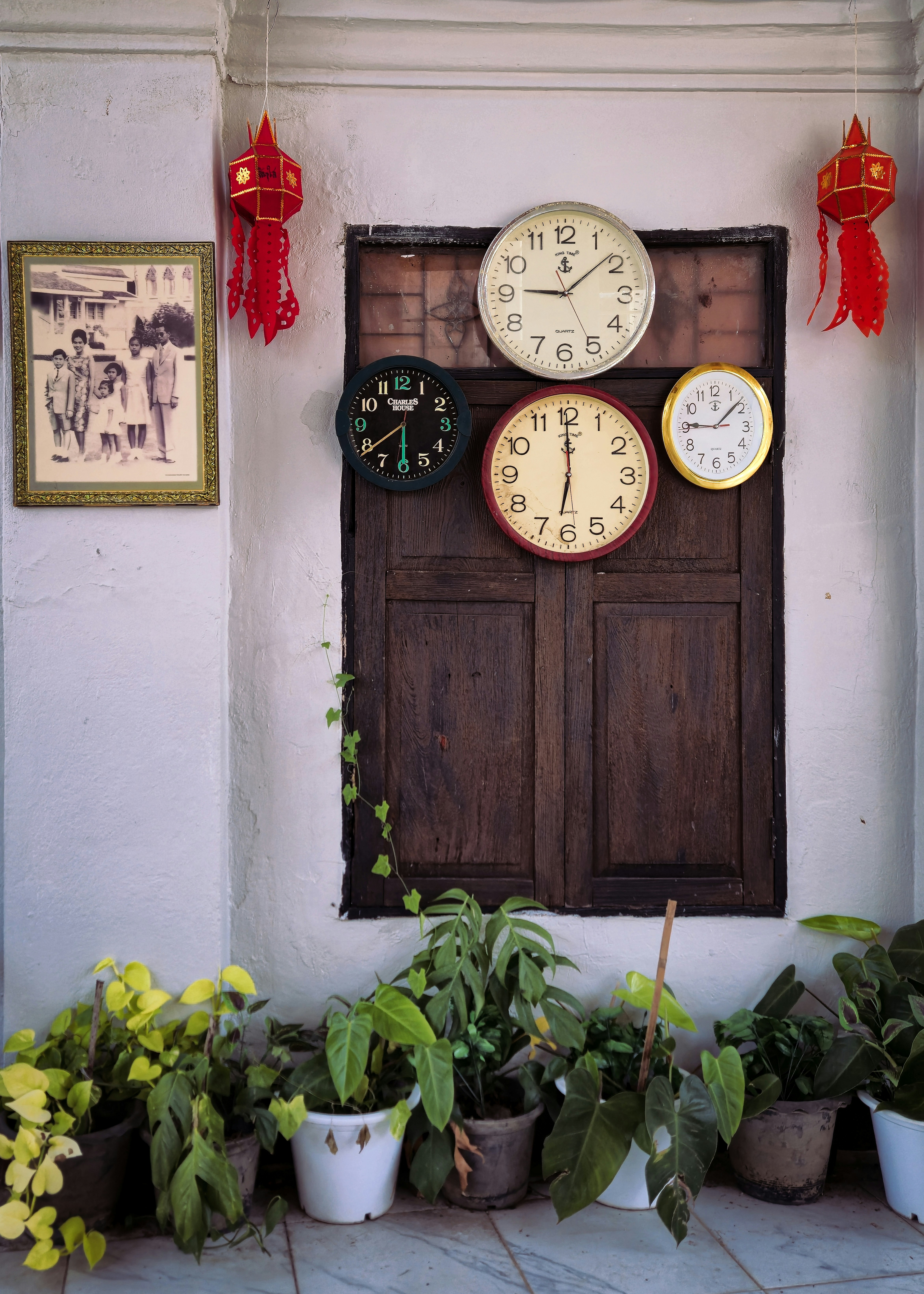 Four clocks hang above a wooden window with plants.