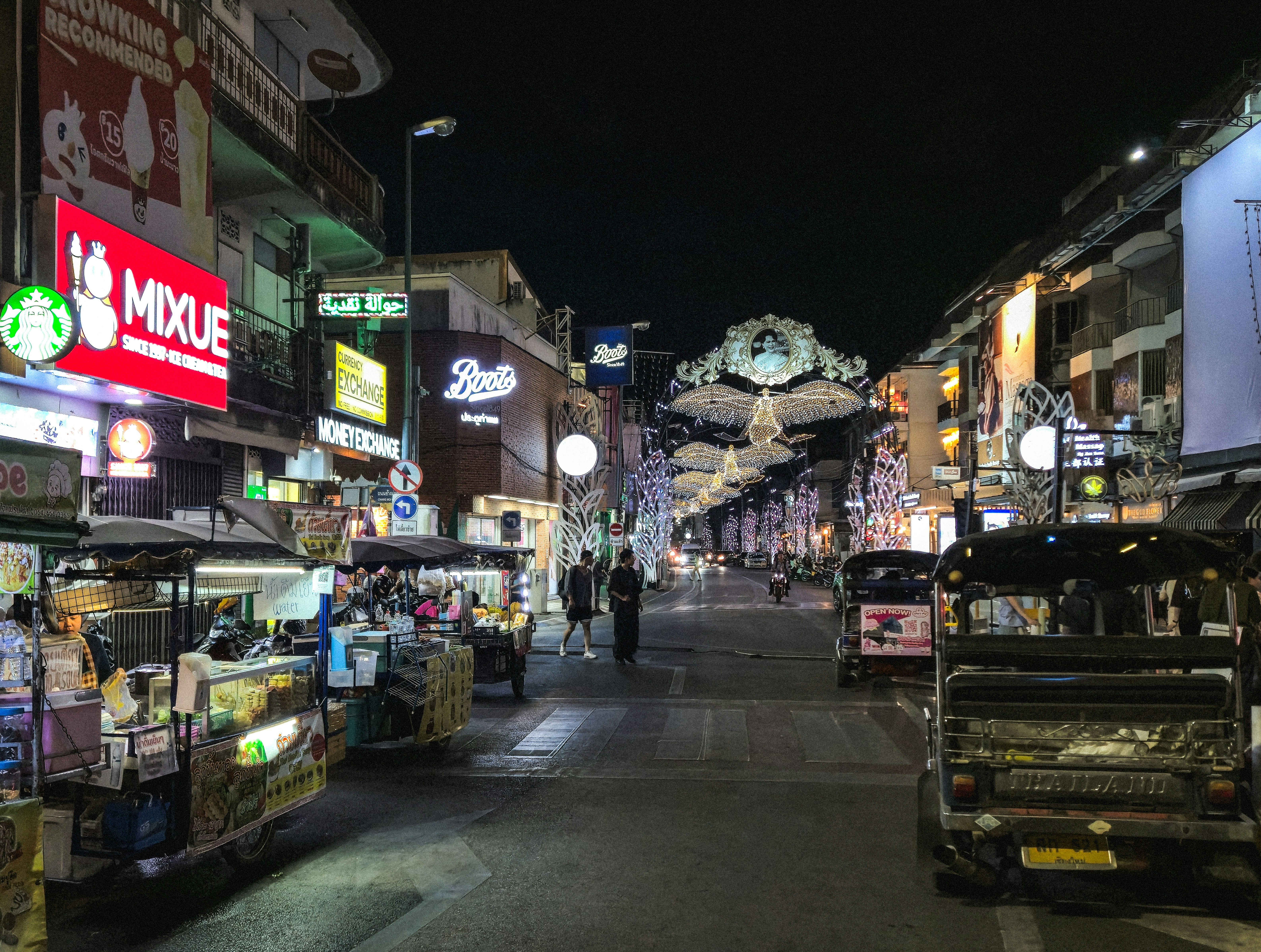 Busy street scene with tuk-tuks and illuminated shops at night.