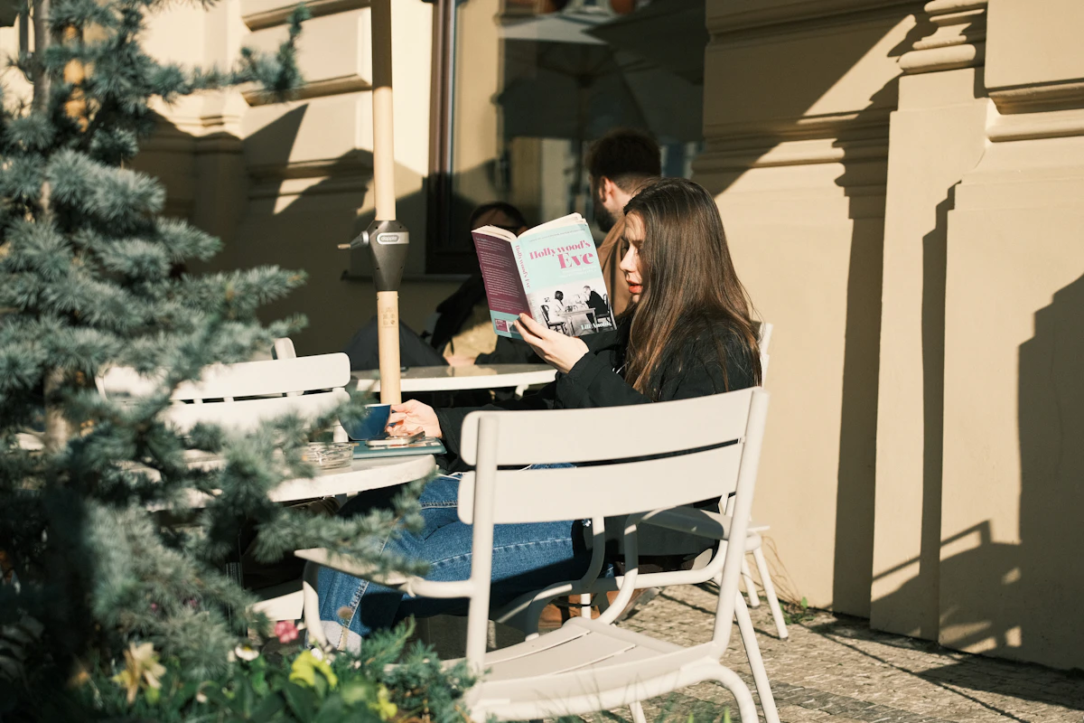 A young woman reading a book alone at an outdoor cafe