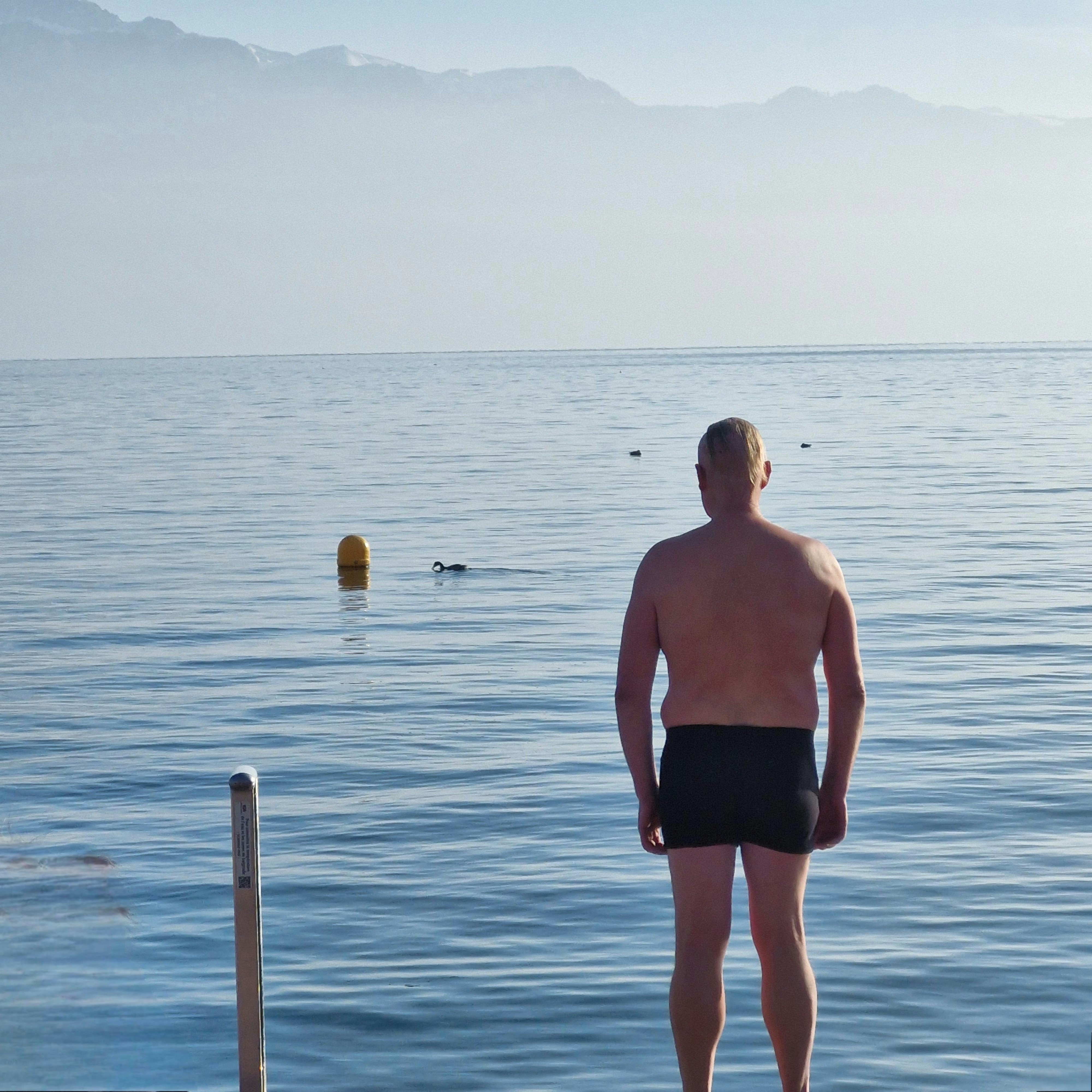 Man standing on dock looking at calm blue lake