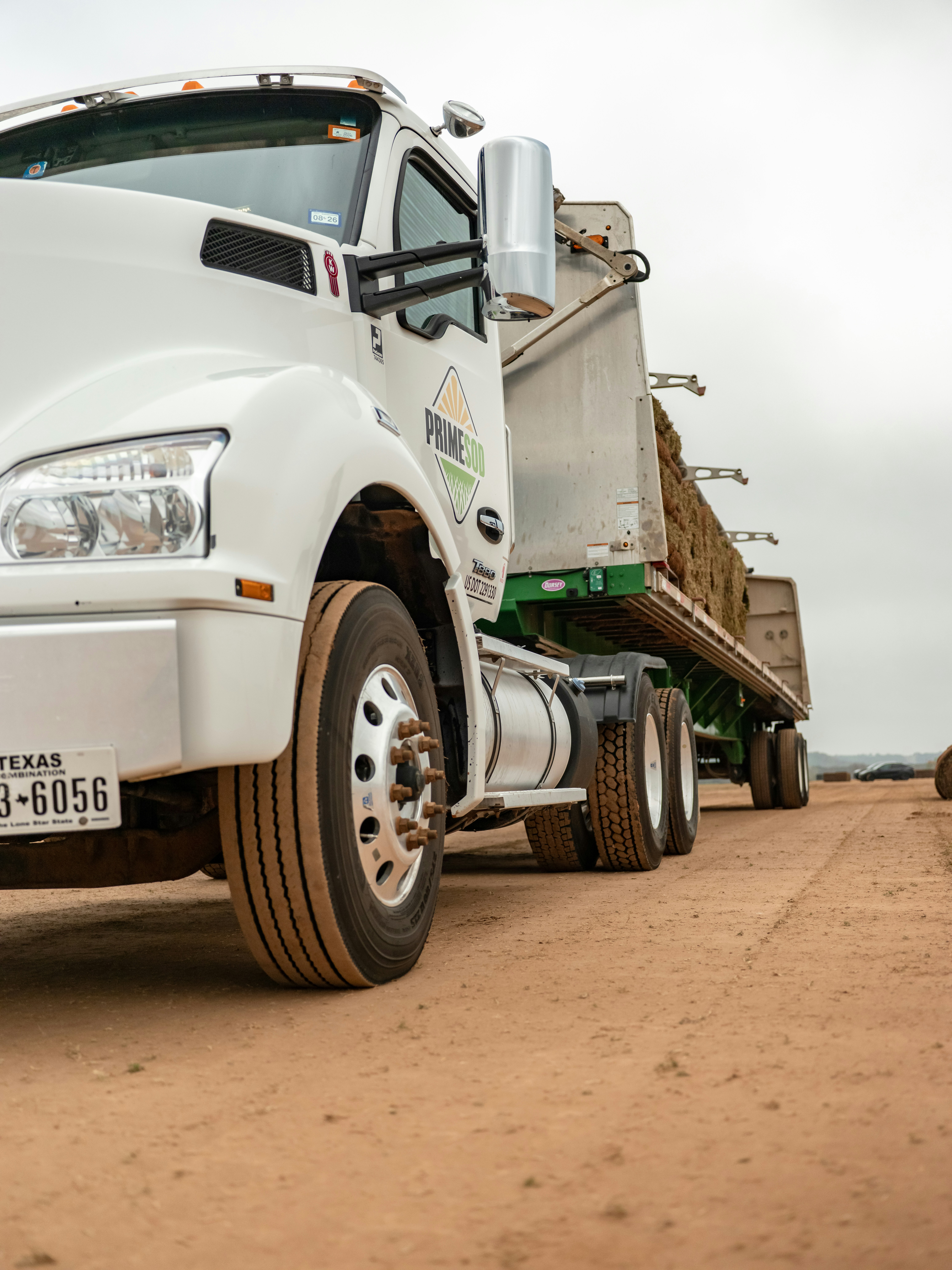 White semi-truck hauling hay bales on a dirt road.