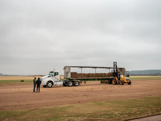 Forklift loading hay bales onto a semi-trailer truck.