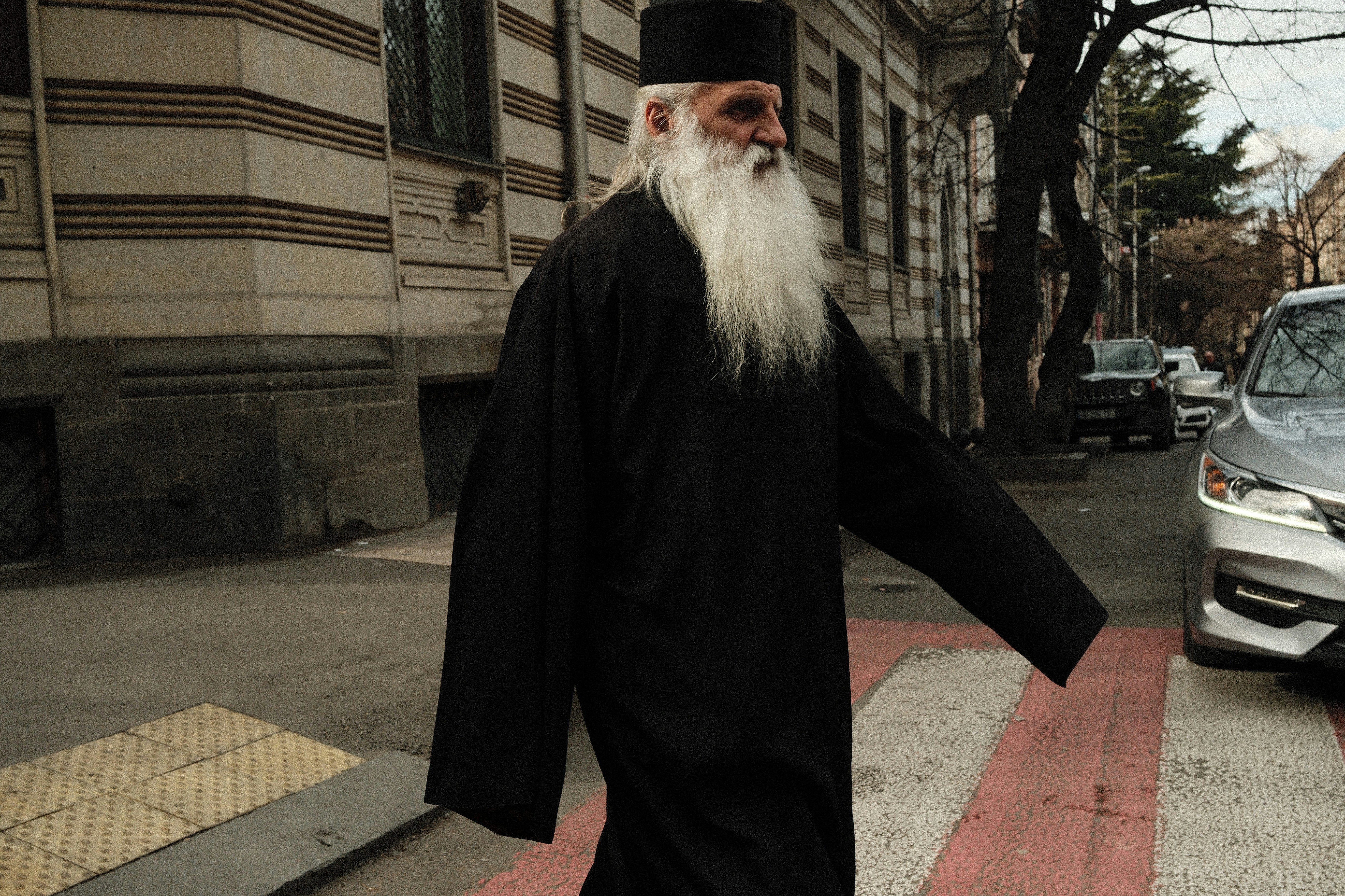 Elderly man in religious attire crossing street.
