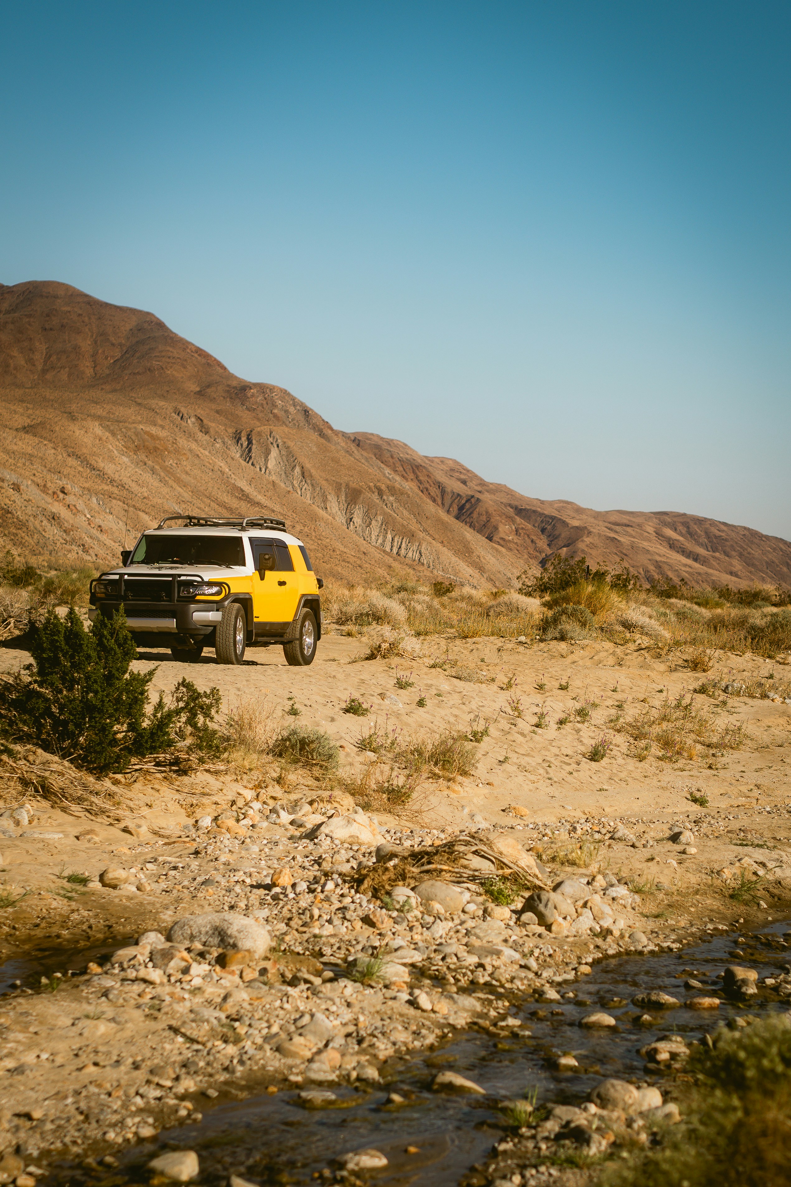 Yellow suv parked in a dry, rocky desert landscape.