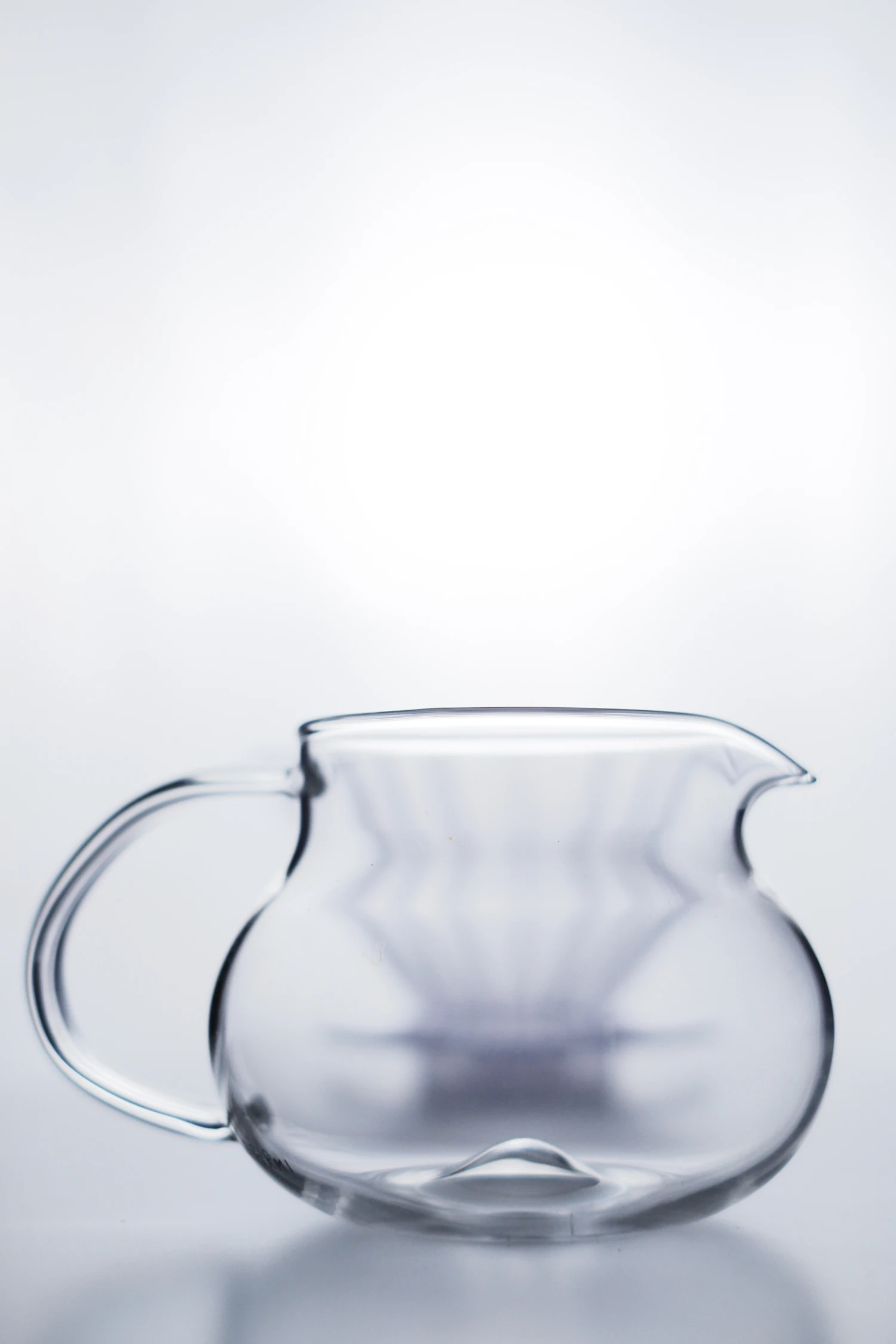 A round clear glass carafe with a loop handle on a white ground