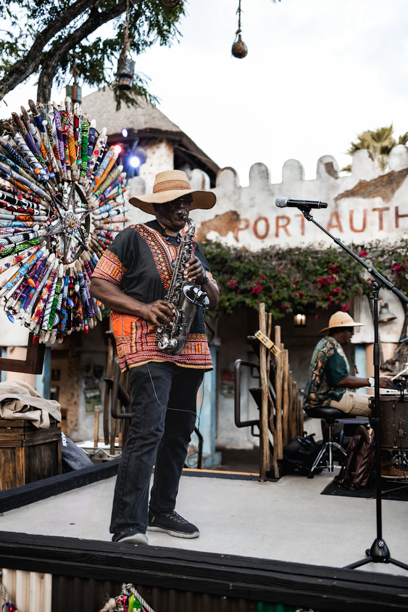 Saxophoniste en chapeau de paille et tunique brodée, jouant sur une scène en plein air.