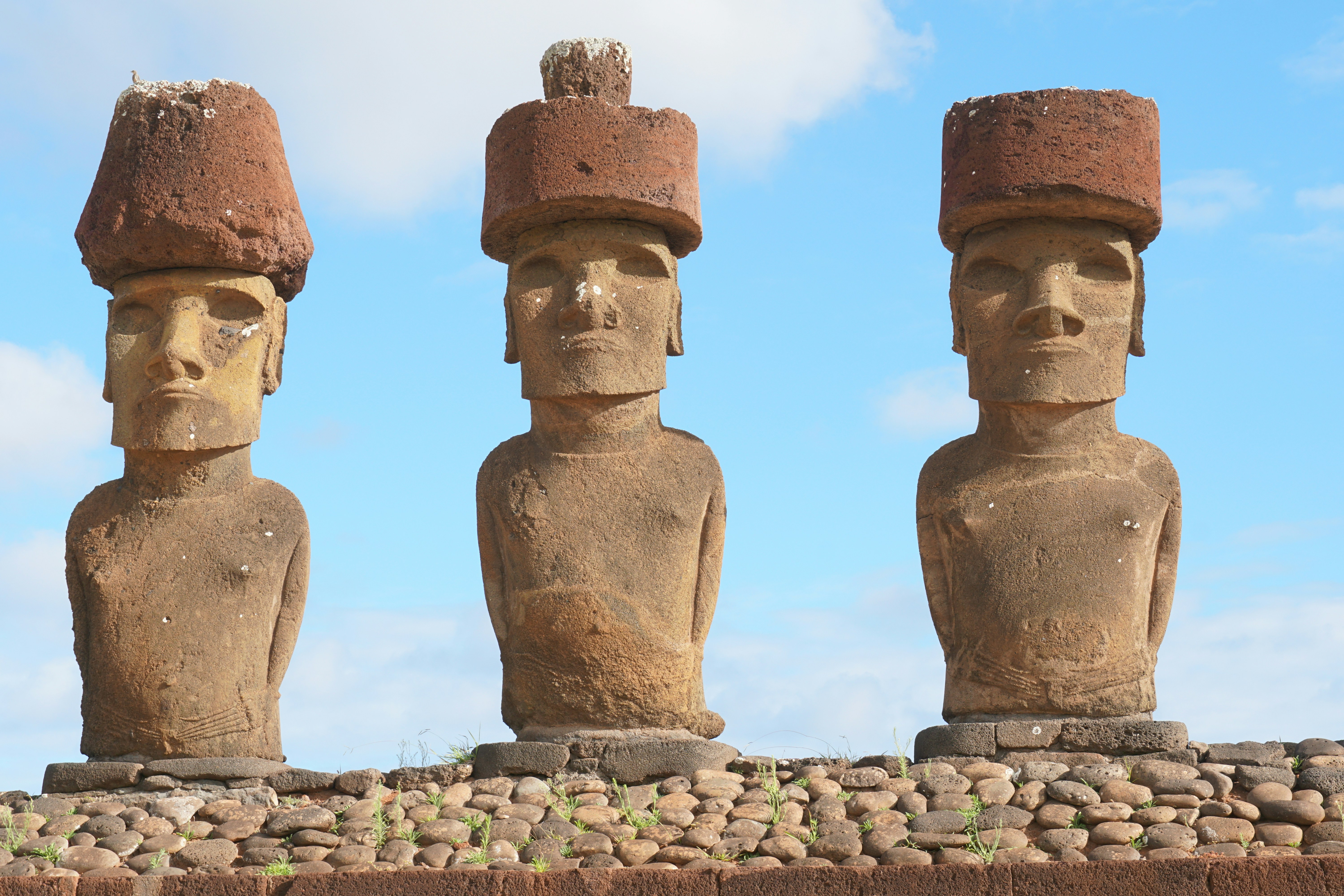 Three moai statues on easter island under a blue sky.