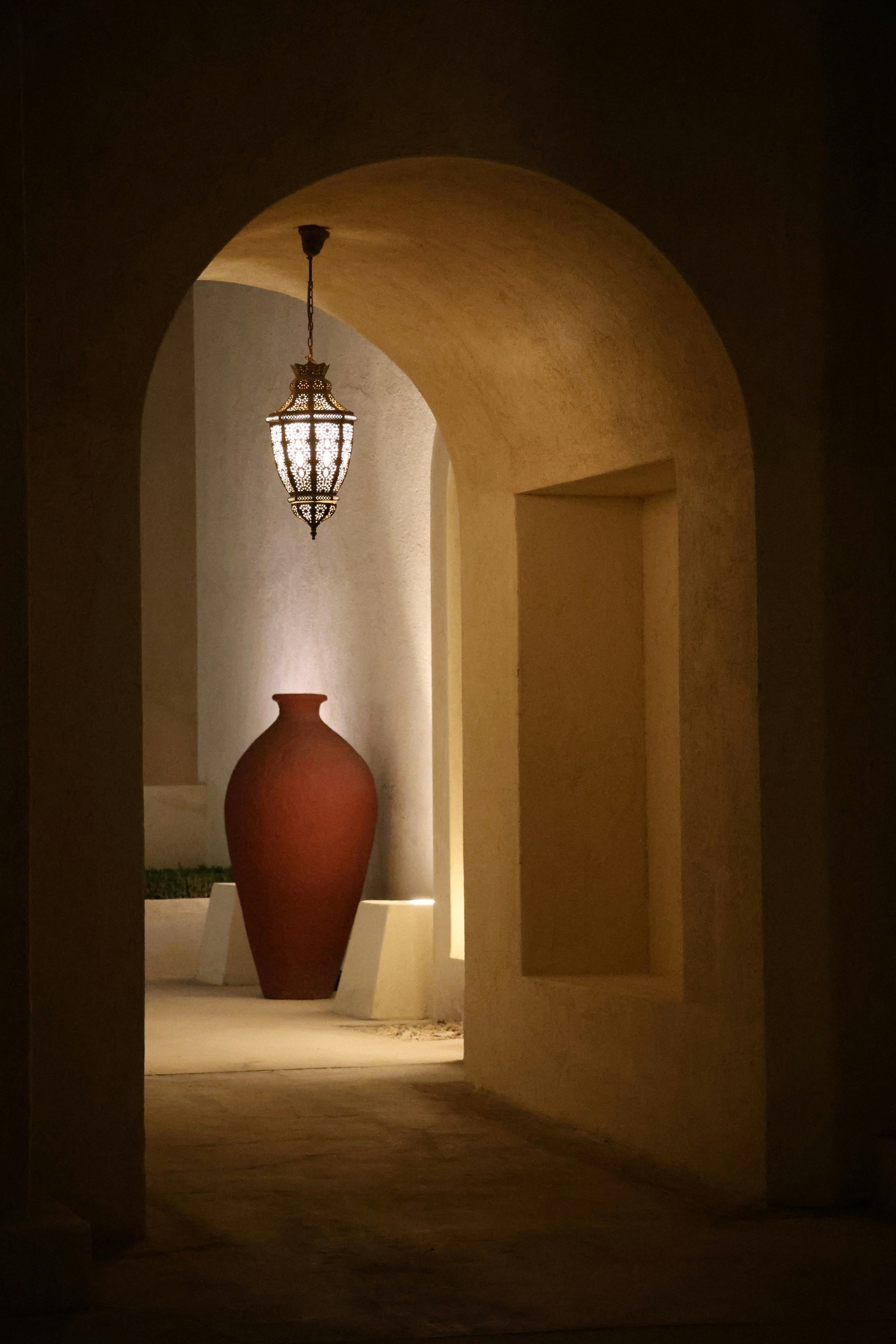 Arched hallway with a large vase and ornate lantern.
