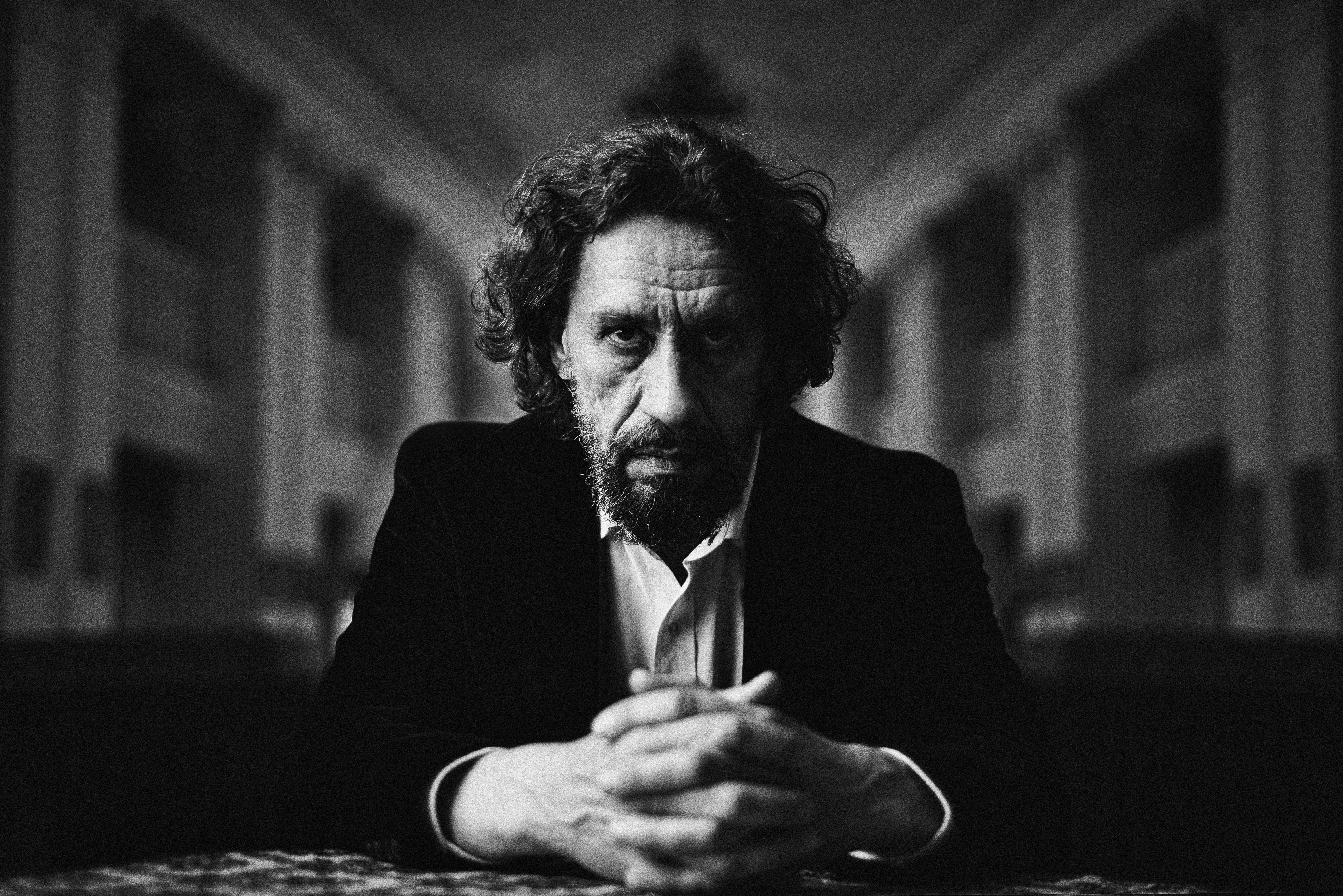 Man with curly hair sits with hands clasped.