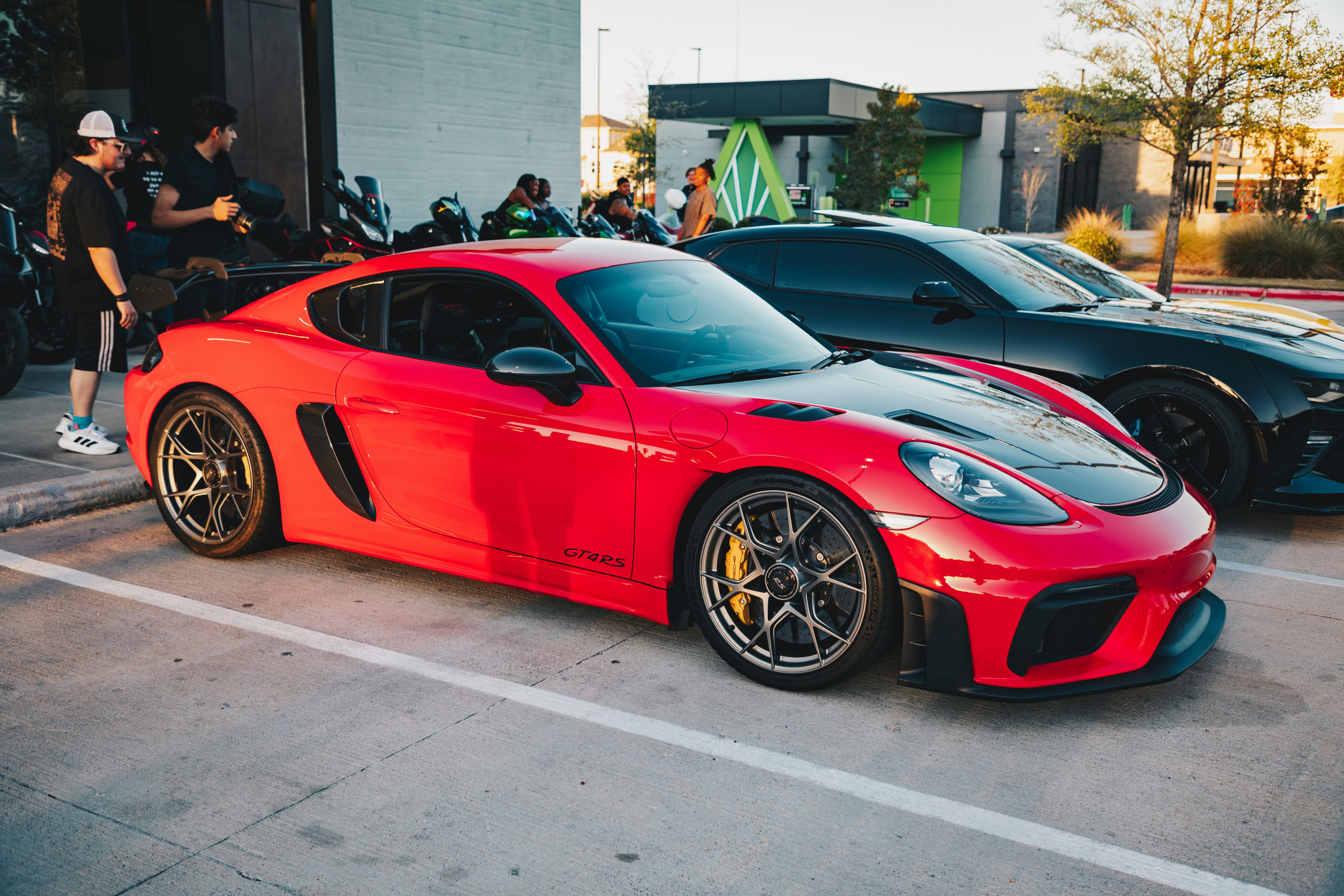 Ein roter Sportwagen steht neben einem dunklen Auto.