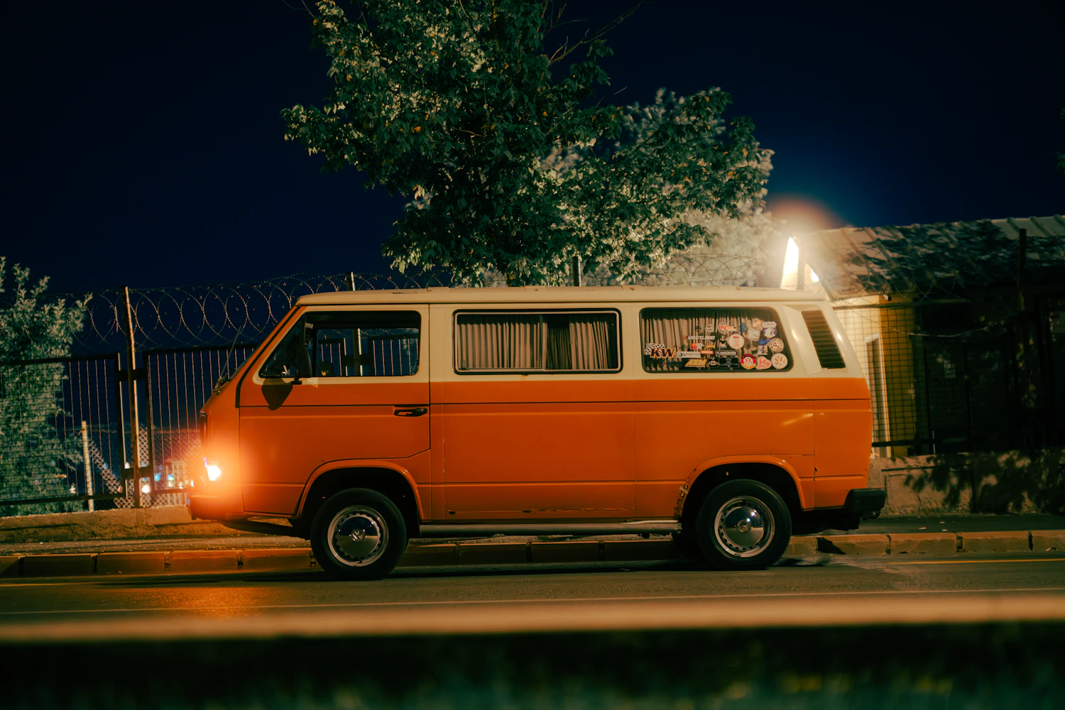 The band van parked at the edge of a field after dark with its lights on