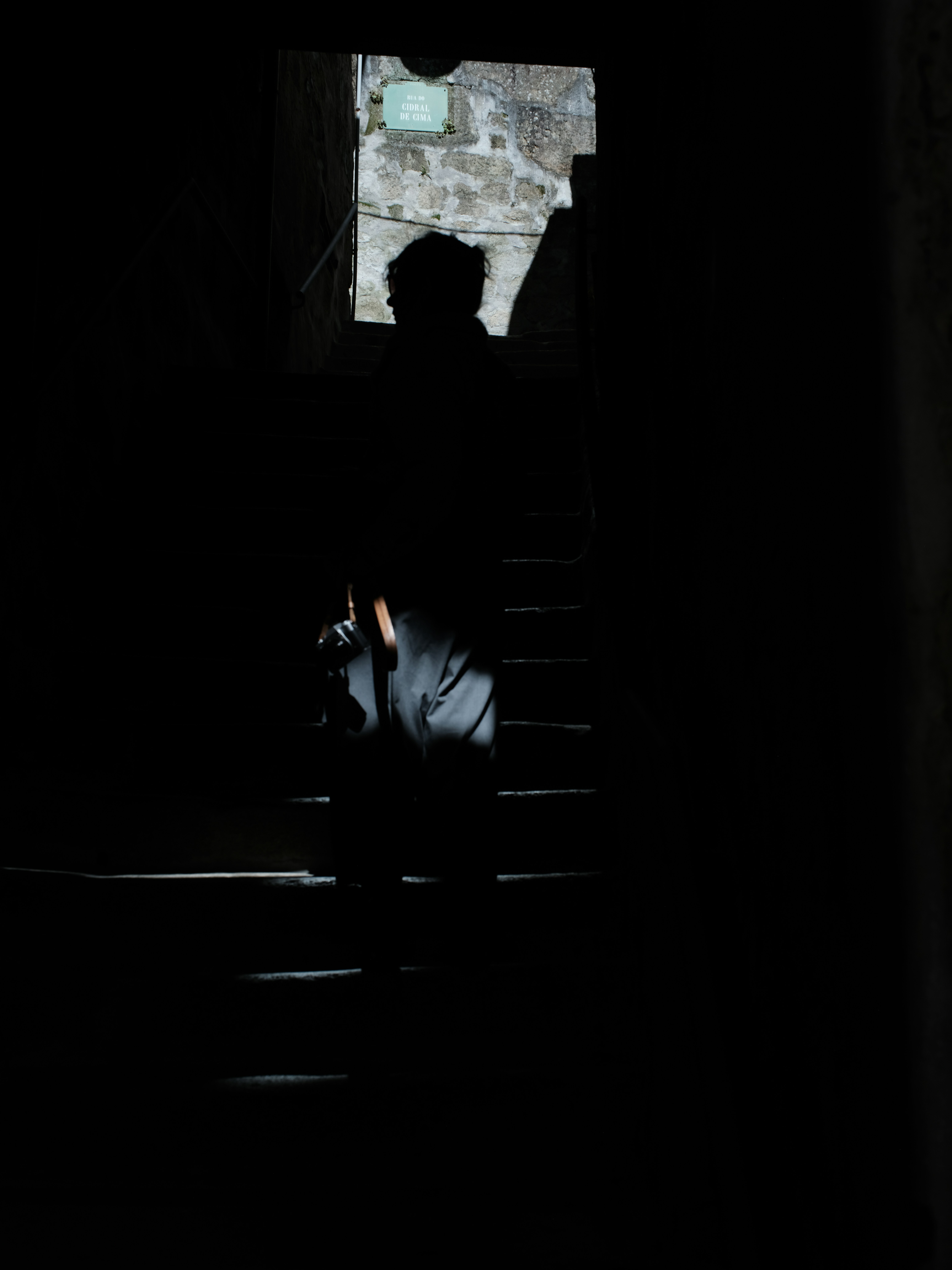 Person walking down dark stairs with light from above.